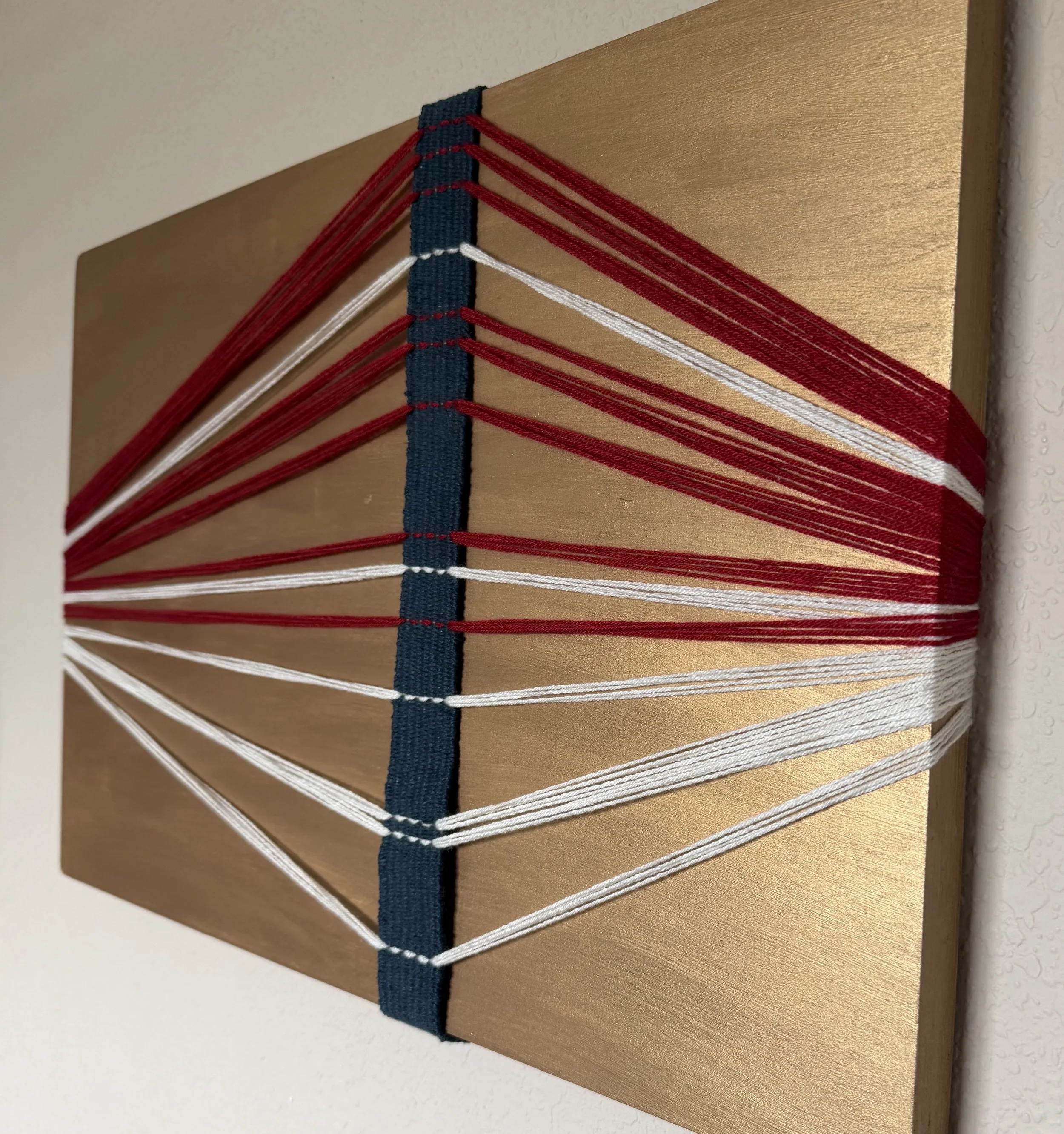 Wooden board with red, white, and blue elastic bands woven in a pattern.