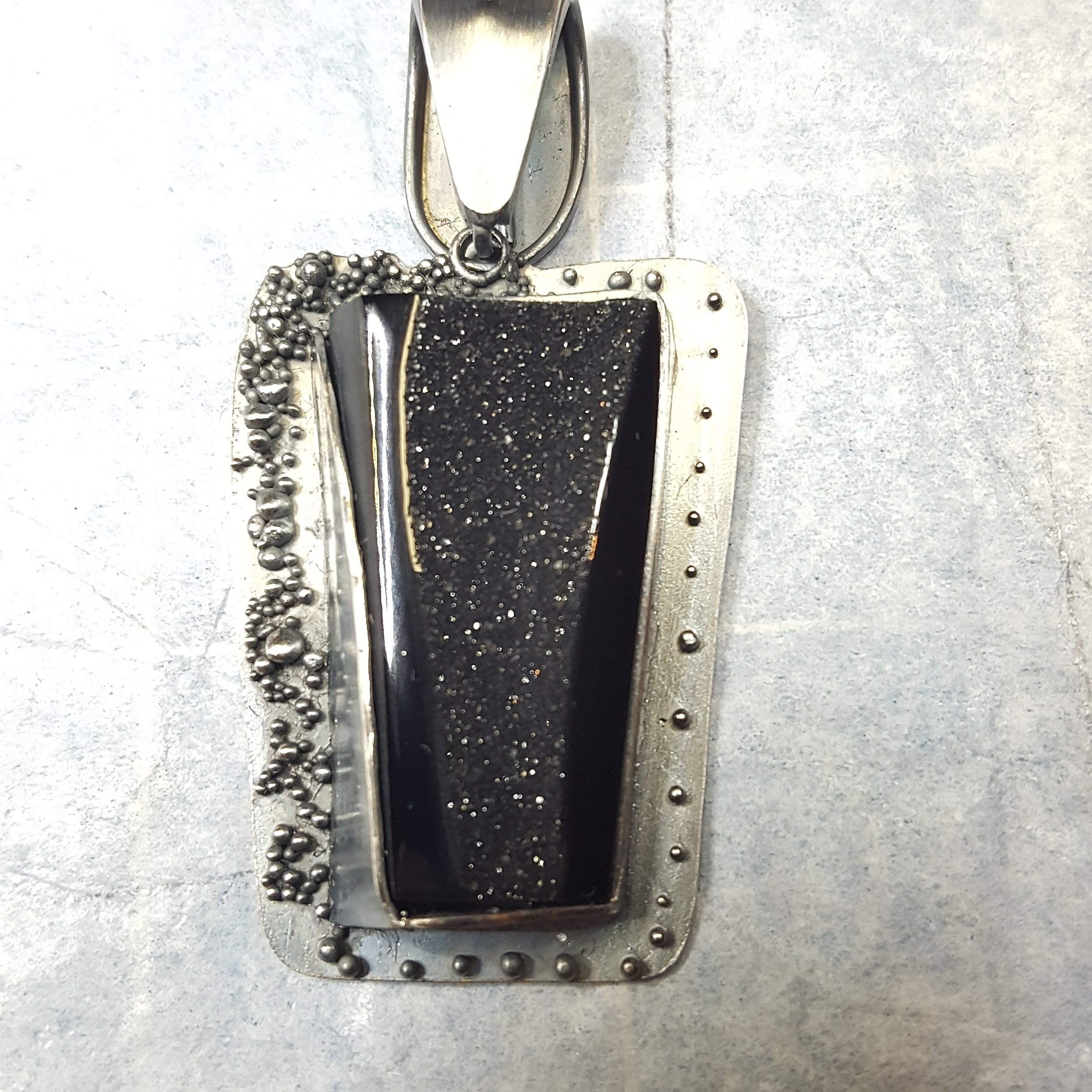 A metal form mold containing black material with tiny sparkles, surrounded by small steel balls and metallic components, on a gray surface.