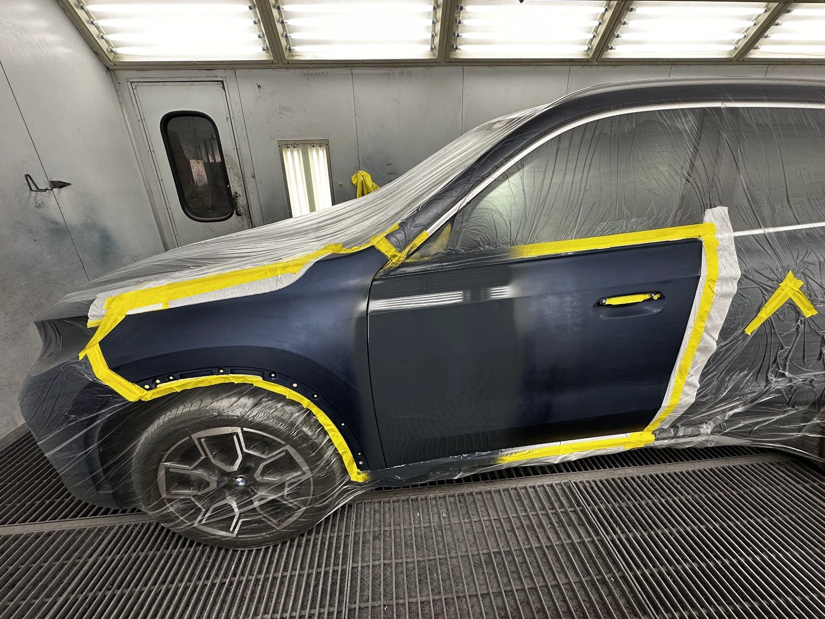A car inside a paint booth covered with protective plastic and tape for a paint job or repair.