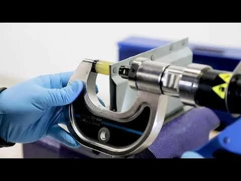 Close-up of a hand in a blue glove holding a small component in a medical or scientific device with a metallic circular part and a yellow marker, in a laboratory setting.