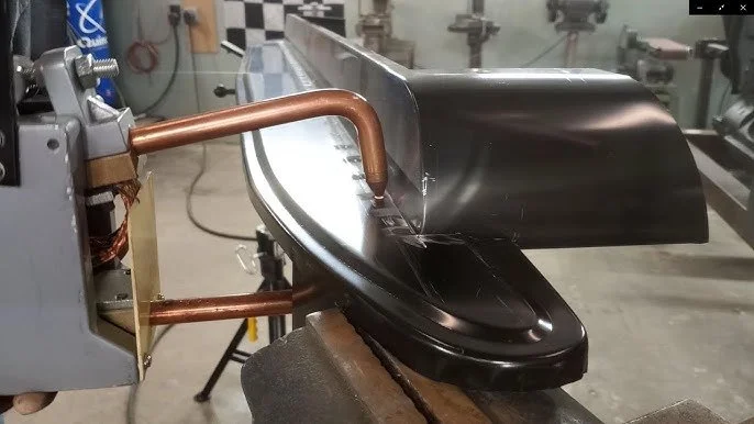 Metalworking machine welding a black guitar body on a workbench.