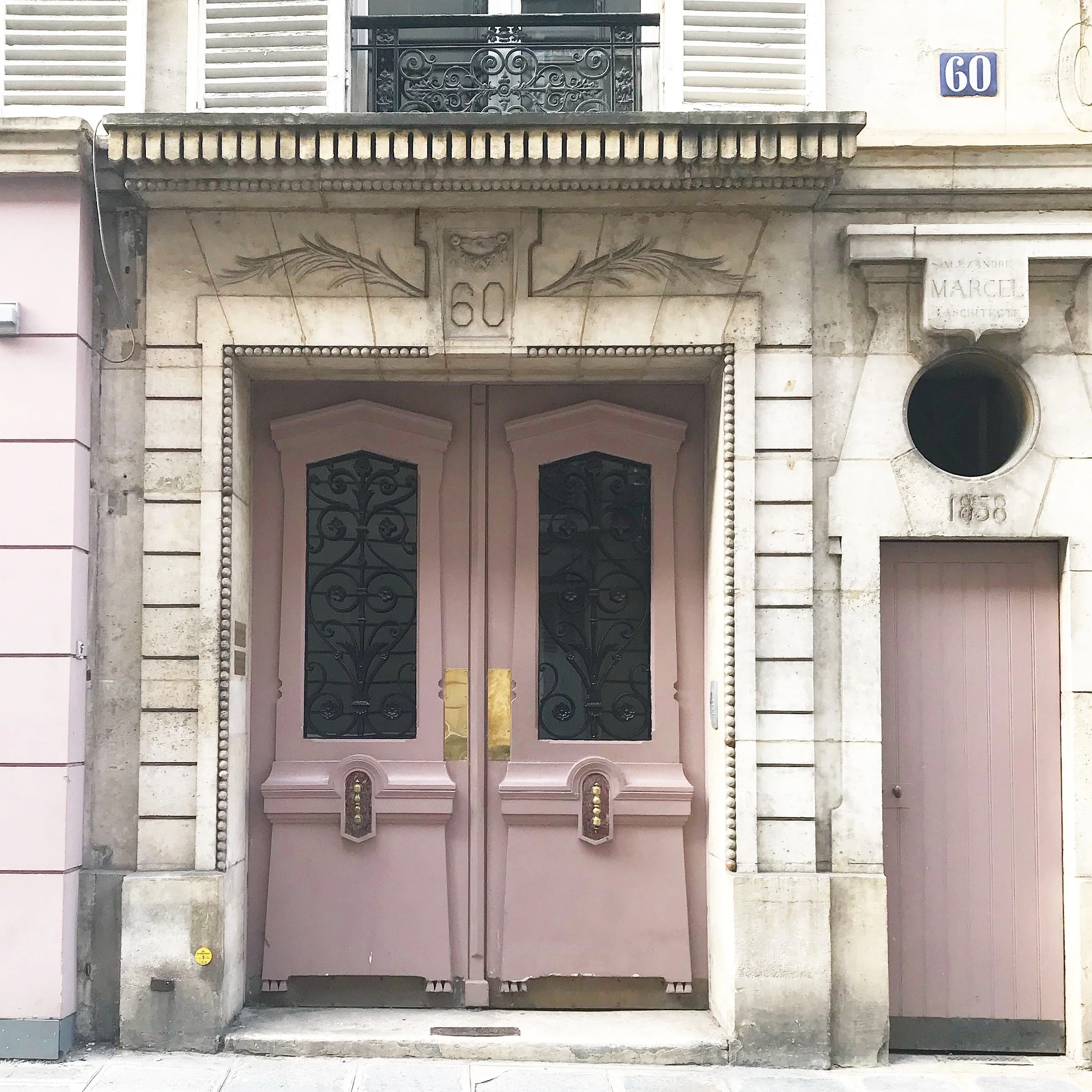 Historical building entrance with stone frame, decorative iron doors, and the number 60 above the door, with a small plaque to the side reading 'ANANDRE MARCEL ARCHITECTURE'.