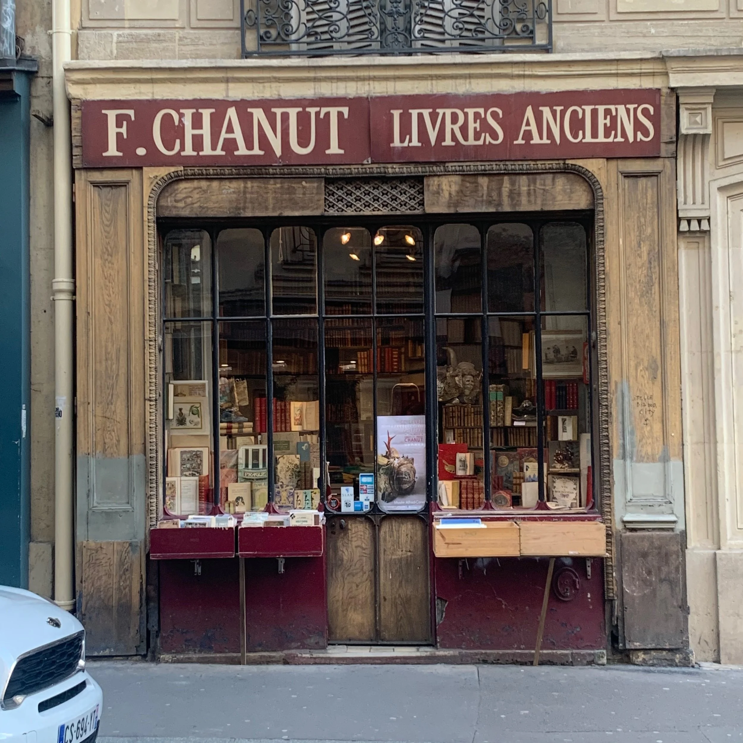 A storefront with a large red sign that reads 'F. CHANTY LIVRES ANCIENS'. The display window showcases various books and artwork, indicating a bookstore.