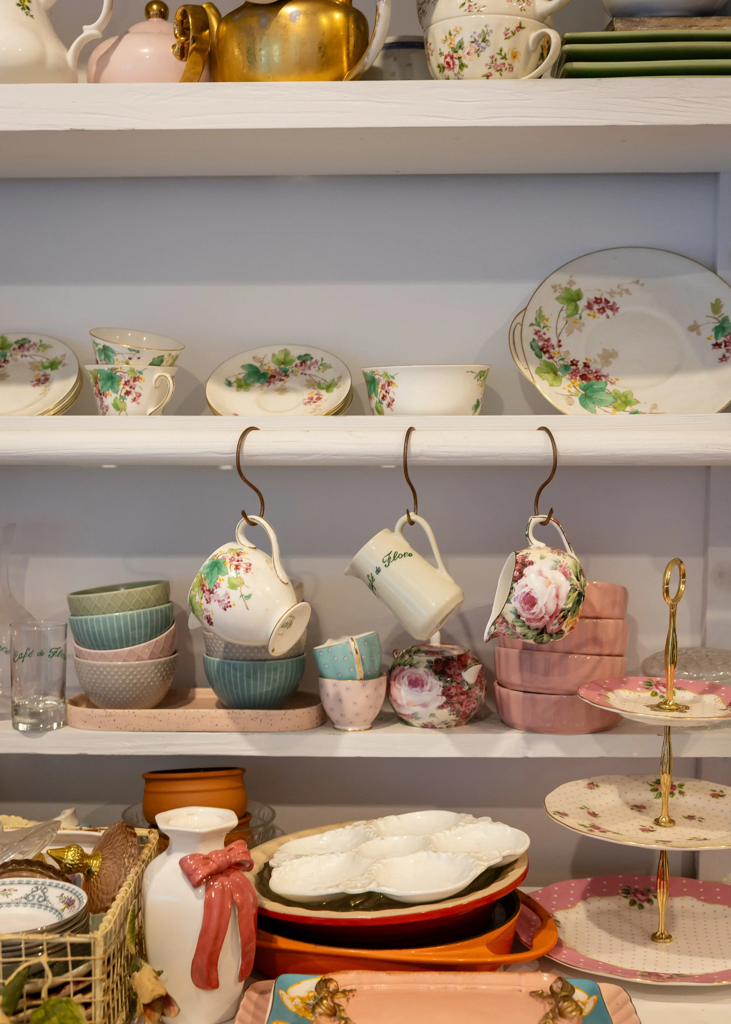 A collection of vintage floral-patterned teacups, saucers, and dishes displayed on shelves and tables, along with a few decorative items like a white porcelain spoon rest and a winking pig figurine.