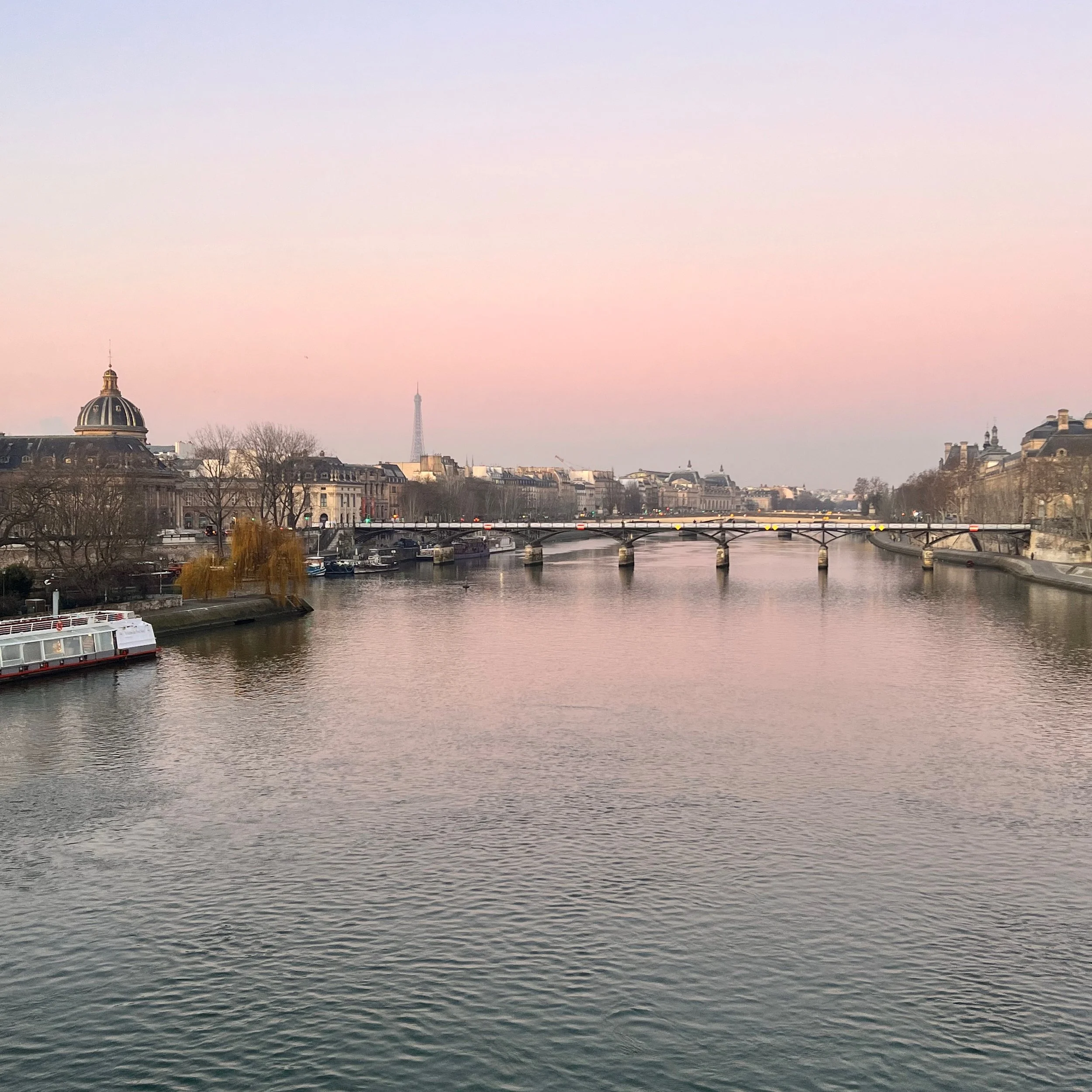 View of the Seine River with bridges, historic buildings, and the Eiffel Tower in the distance during twilight in Paris.