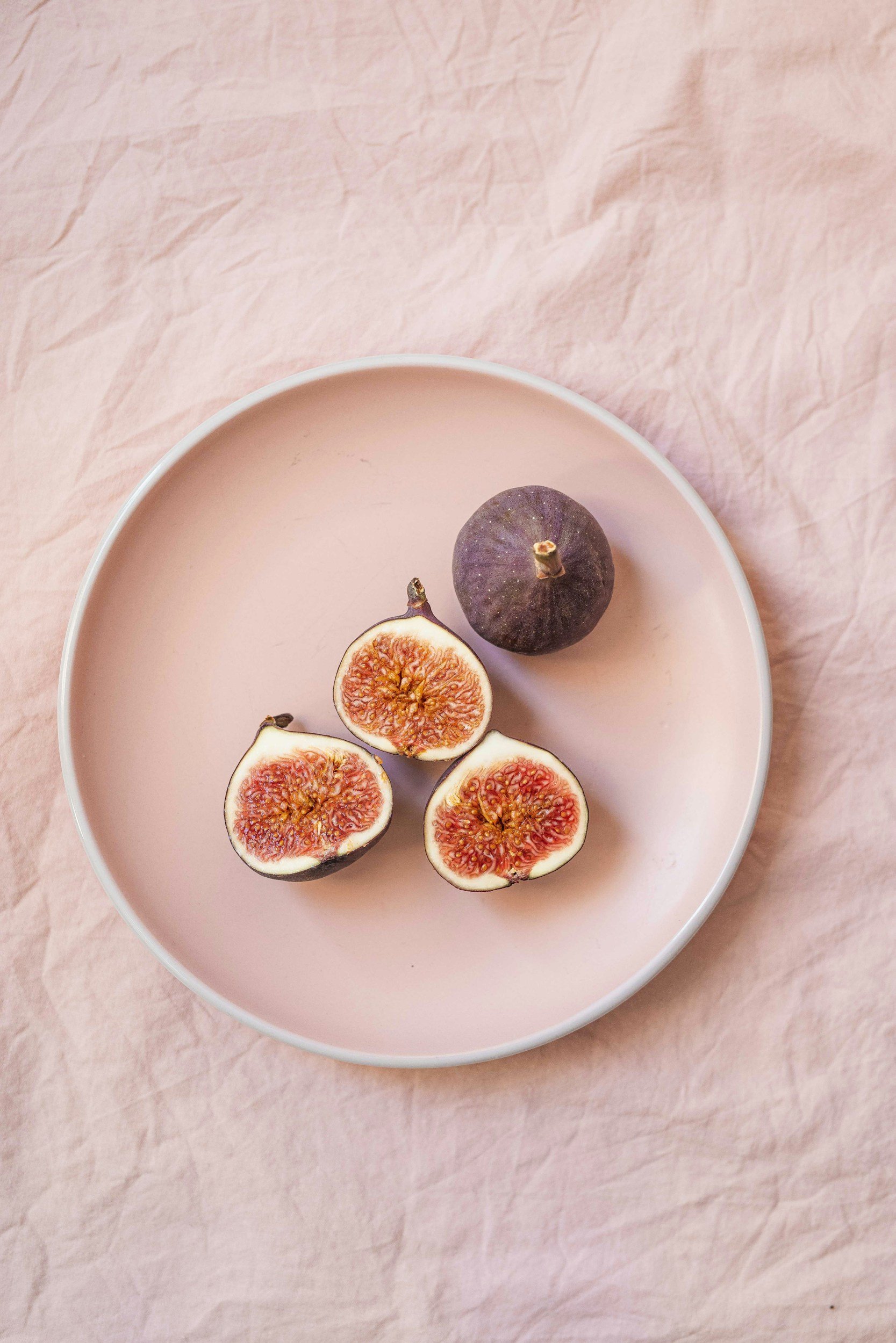 A white plate with slices of fresh figs on a pink textured surface.