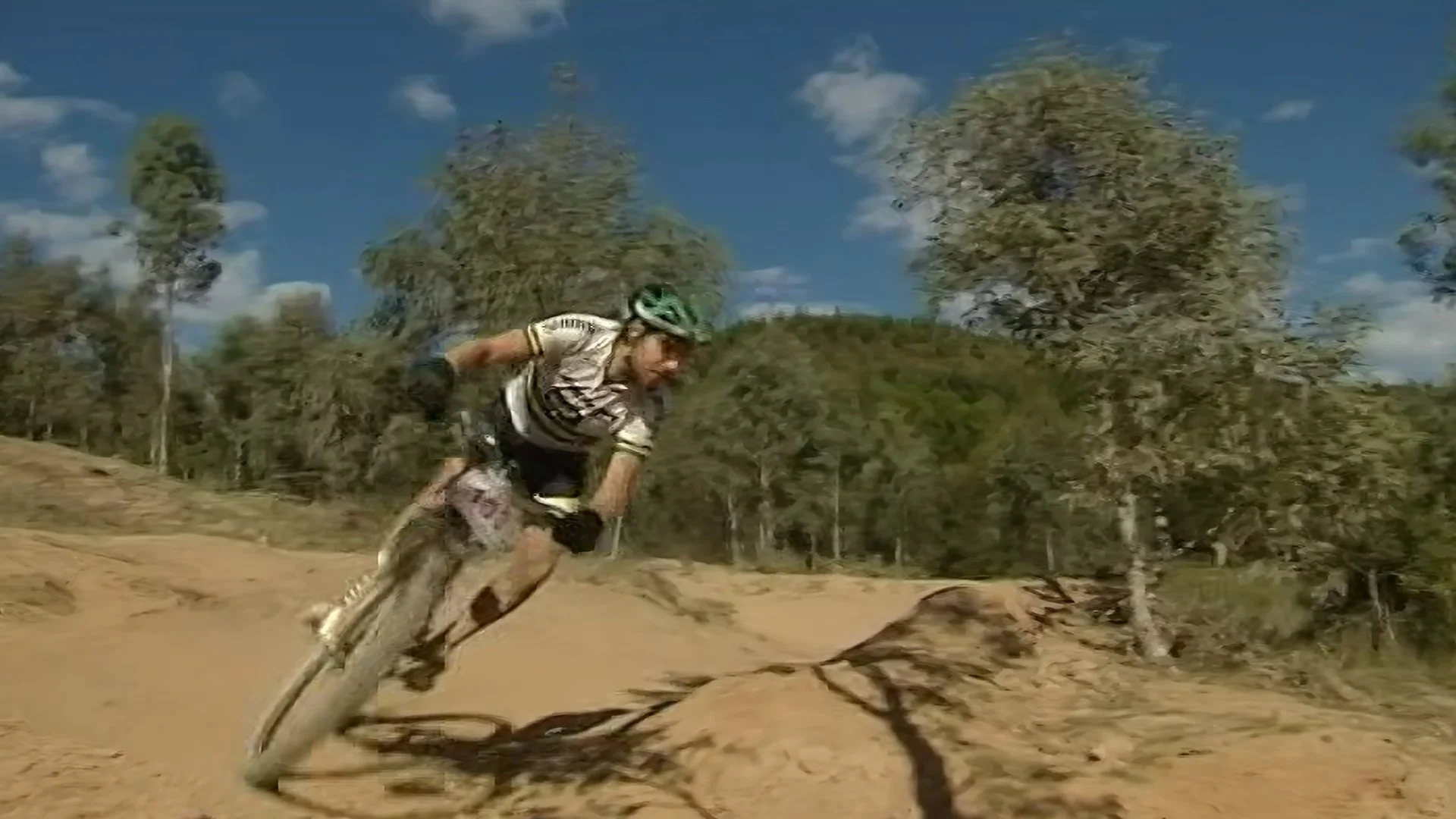 A person riding a dirt bike on a trail through a forested area with trees under a blue sky with clouds.