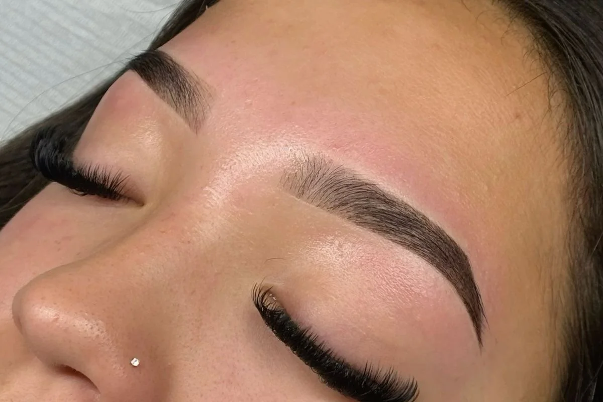 Close-up of a woman with well-groomed eyebrows, long eyelashes, and a small nose stud, lying with eyes closed.