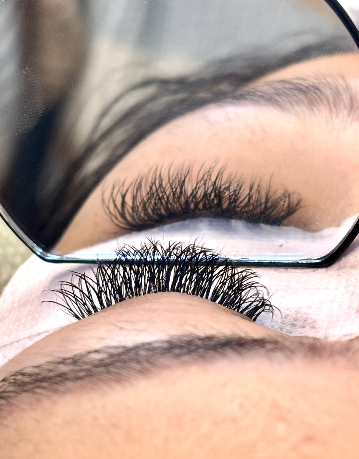 Close-up of a person's eye with long, curled eyelashes and well-groomed eyebrows, reflected in a mirror.
