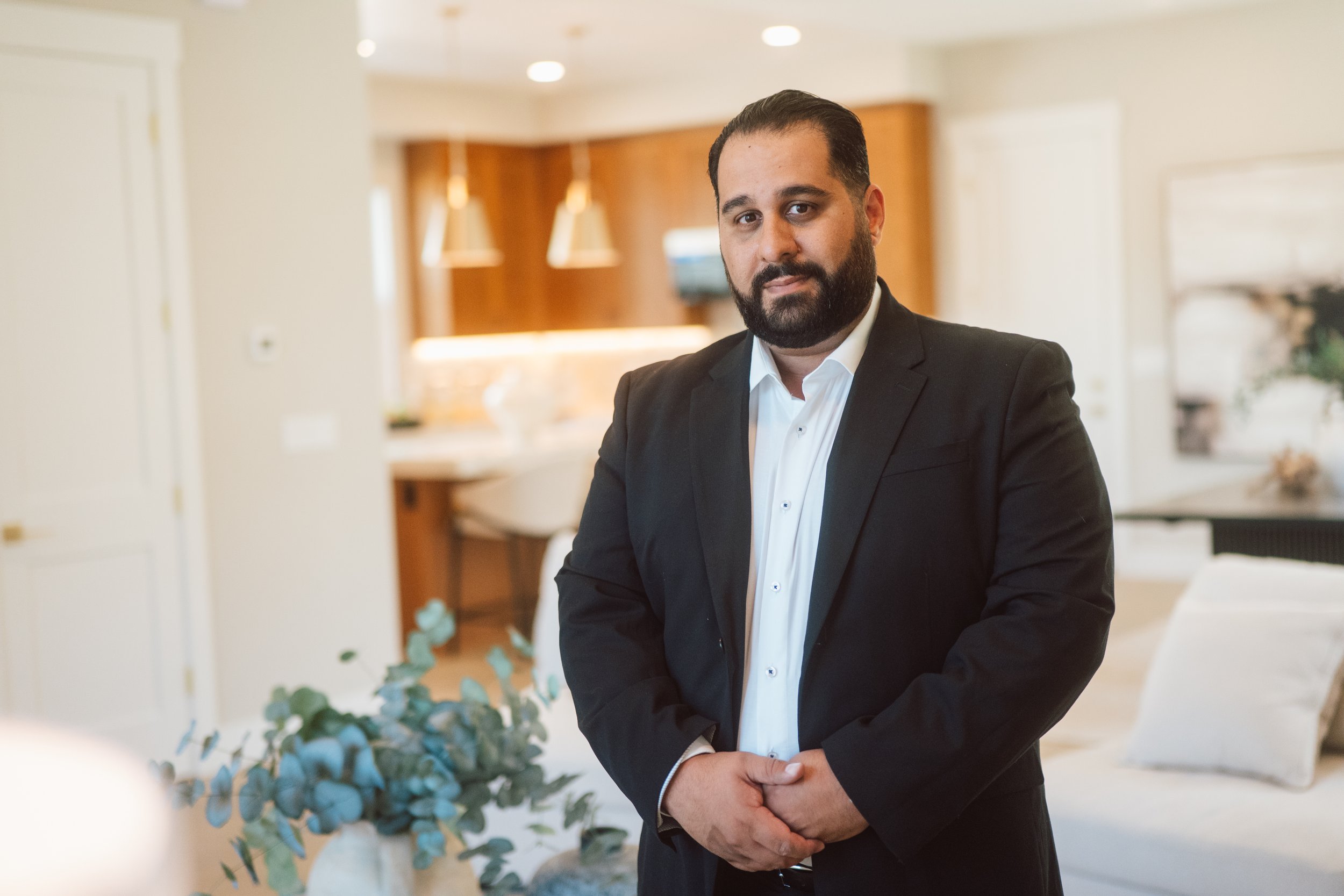 Suroosh Rezaee in a suit inside a living room with the kitchen in the background.