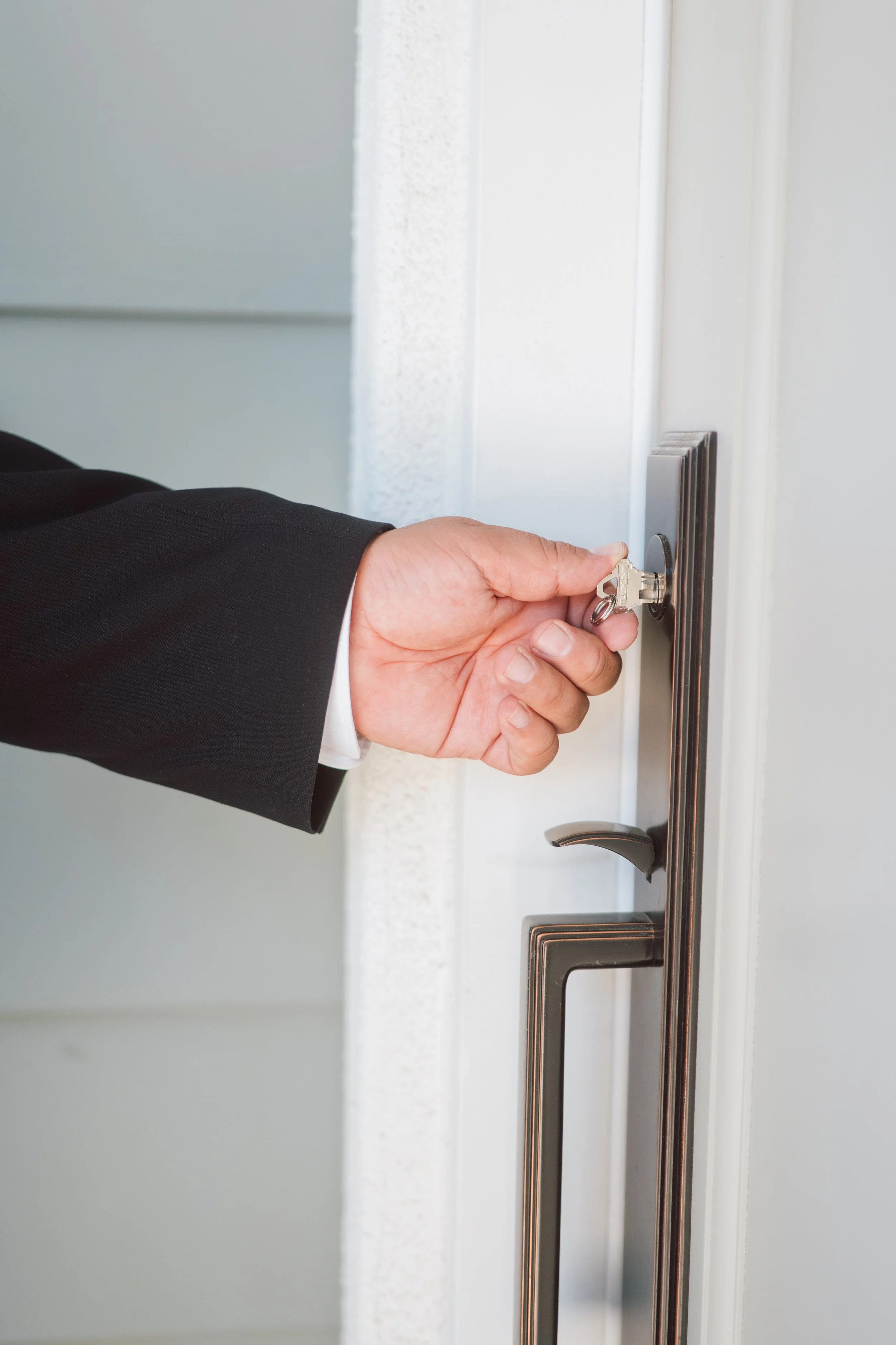 Person in a black suit turning a key in a door lock.