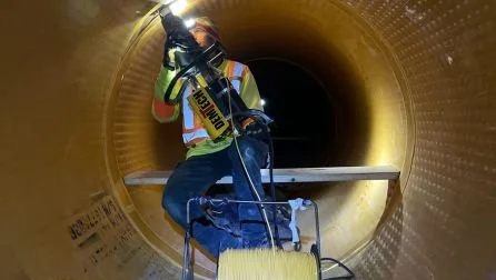 Technician in hi-vis working on liner seams inside an HDPE-lined concrete pipe