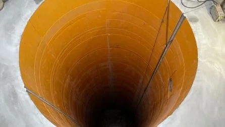 View down a vertical shaft lined with orange HDPE concrete protection liner