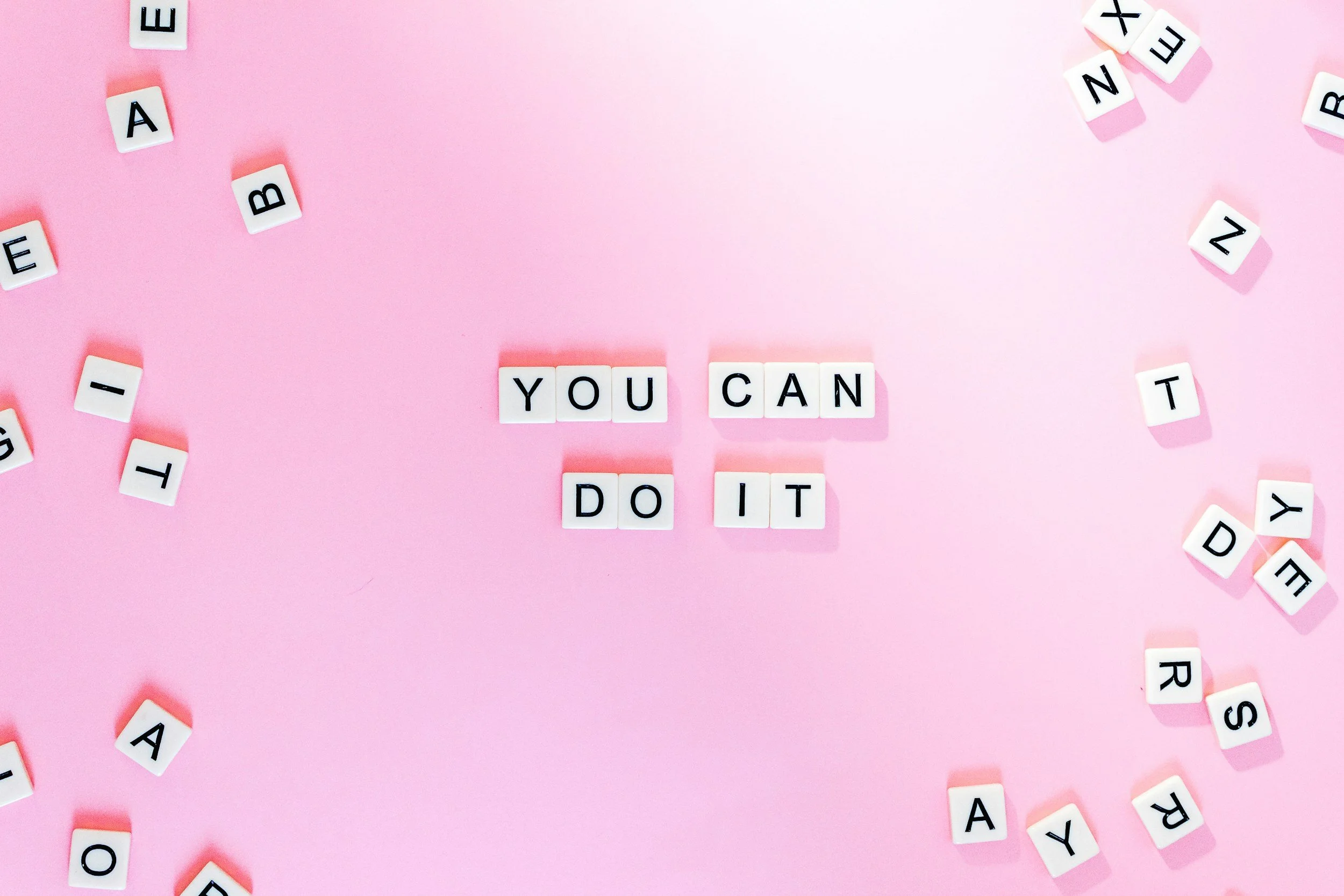 Pink background with white letter tiles displaying the phrase 'YOU CAN DO IT' in the center, surrounded by scattered individual letter tiles.