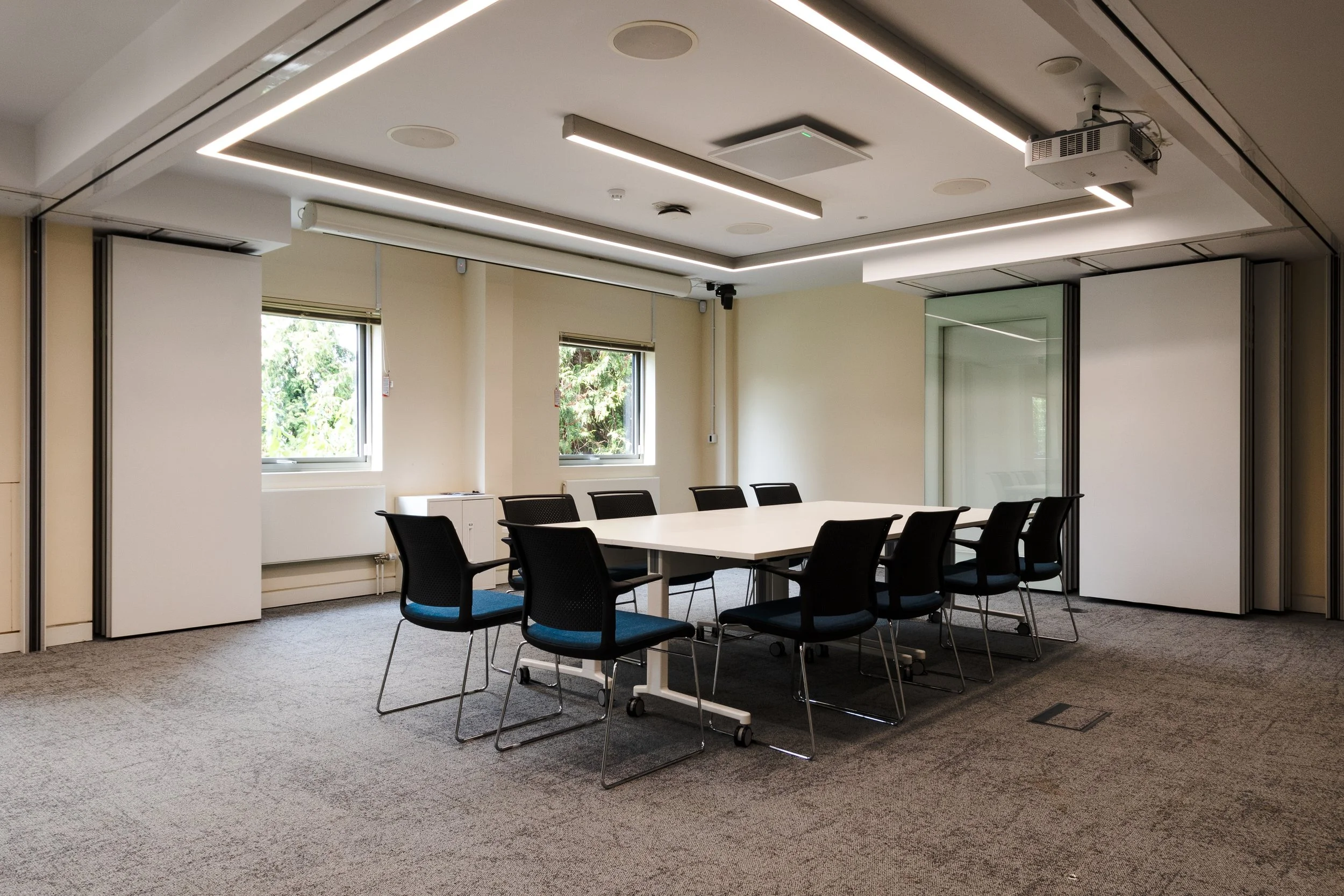 Conference room with a long table, black chairs, windows with blinds, and ceiling lights.
