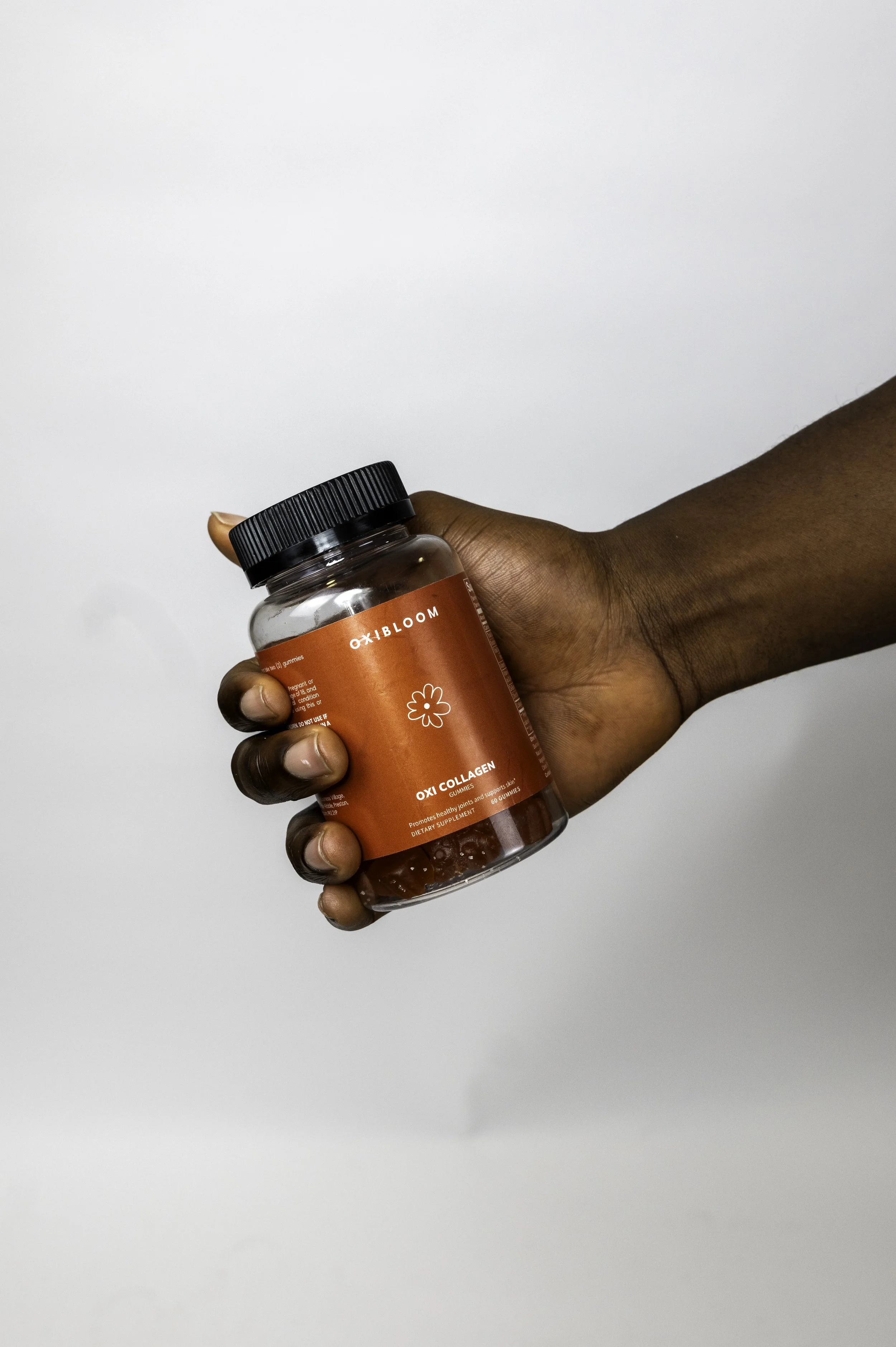 Close-up of a person's hand holding a red bottle labeled 'OXIBLOOM' with a black cap, against a plain white background.