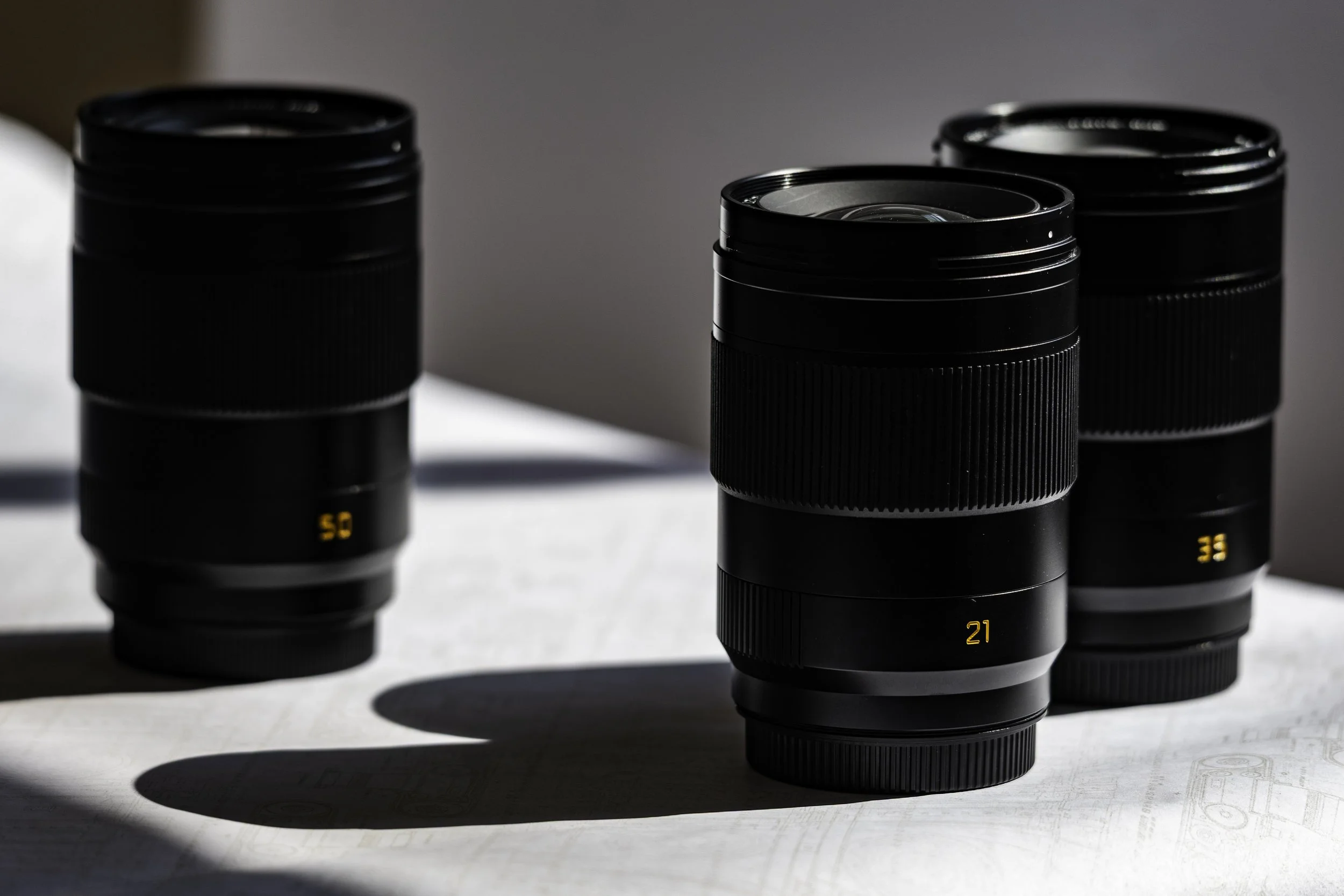Close-up of black camera lenses with numeric focus markings on a white surface, casting shadows.