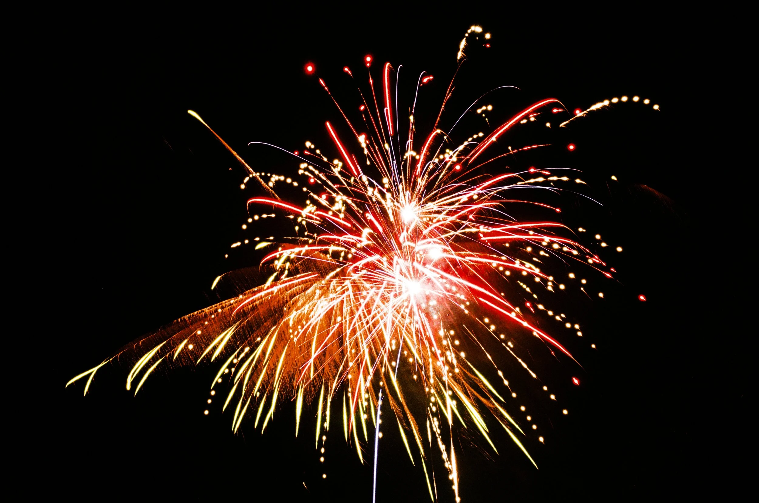 Fireworks exploding in the night sky with bright red, yellow, and white streaks and dots.