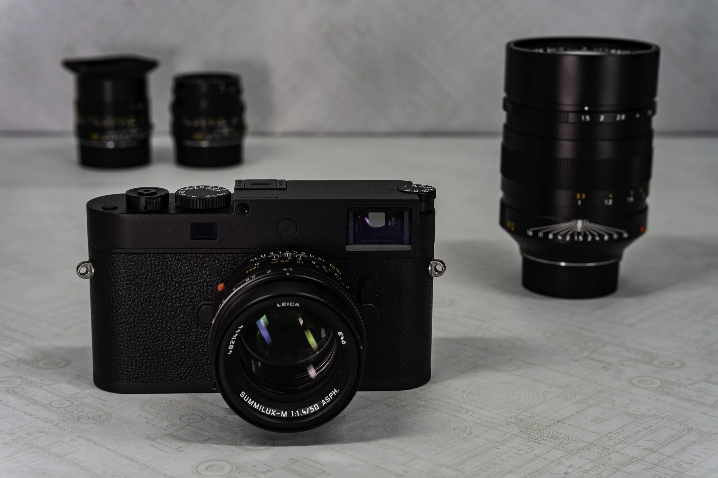 A digital camera with a black body and Leica branding, a focus ring, and a viewfinder lens, positioned on a flat surface.