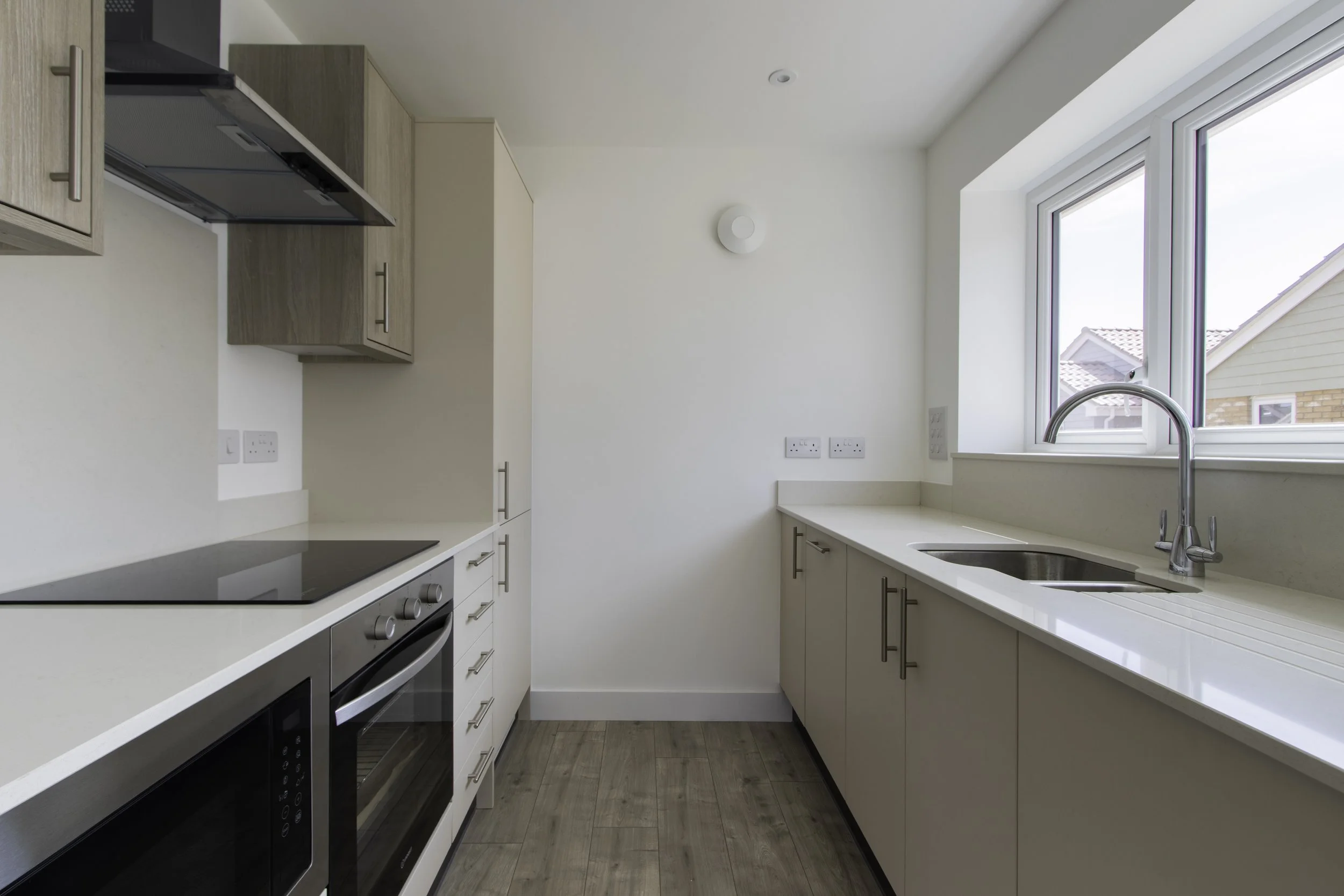 Modern kitchen with white cabinets, black and stainless steel appliances, a large window, and wood flooring.