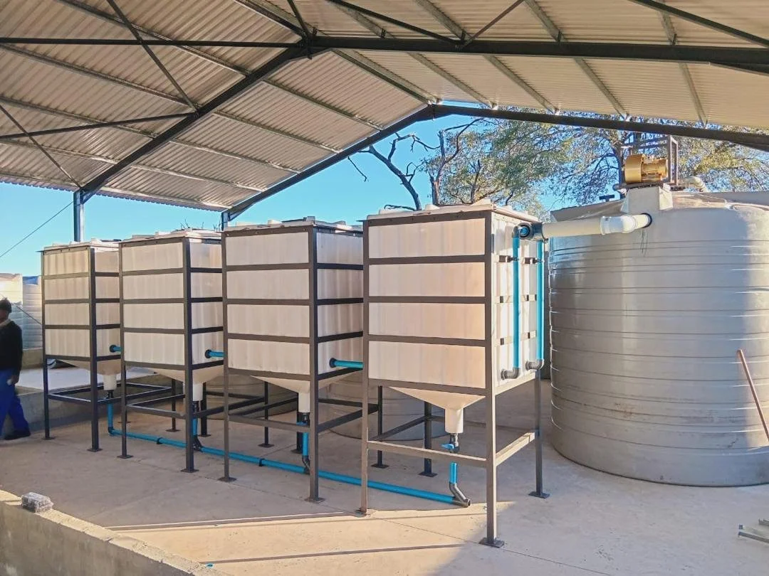 Industrial water filtration or storage tanks under a metal roof structure in an outdoor setting.