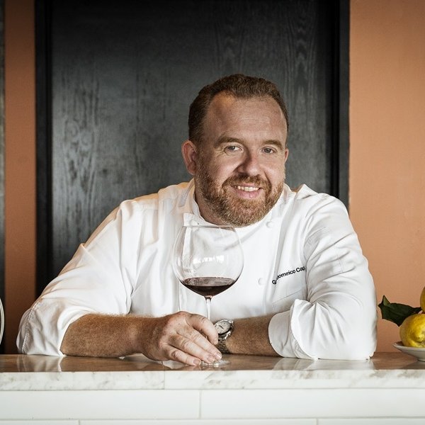 Chef Gianni Caprioli holding a glass of red wine at Giando.