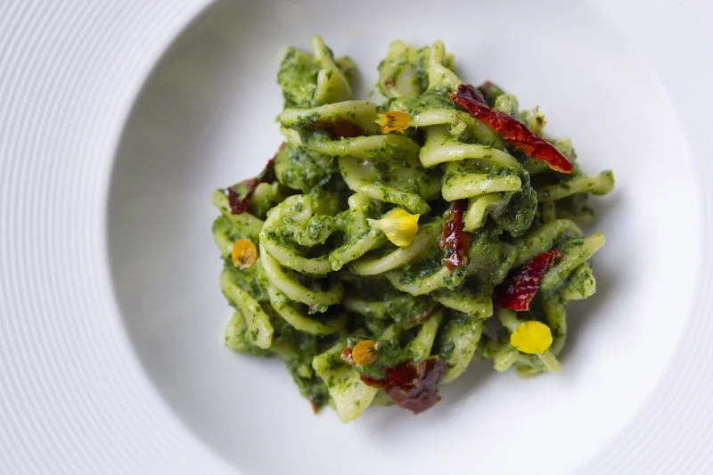 Authentic Italian pesto pasta garnished with red chili and edible flowers at Giando.