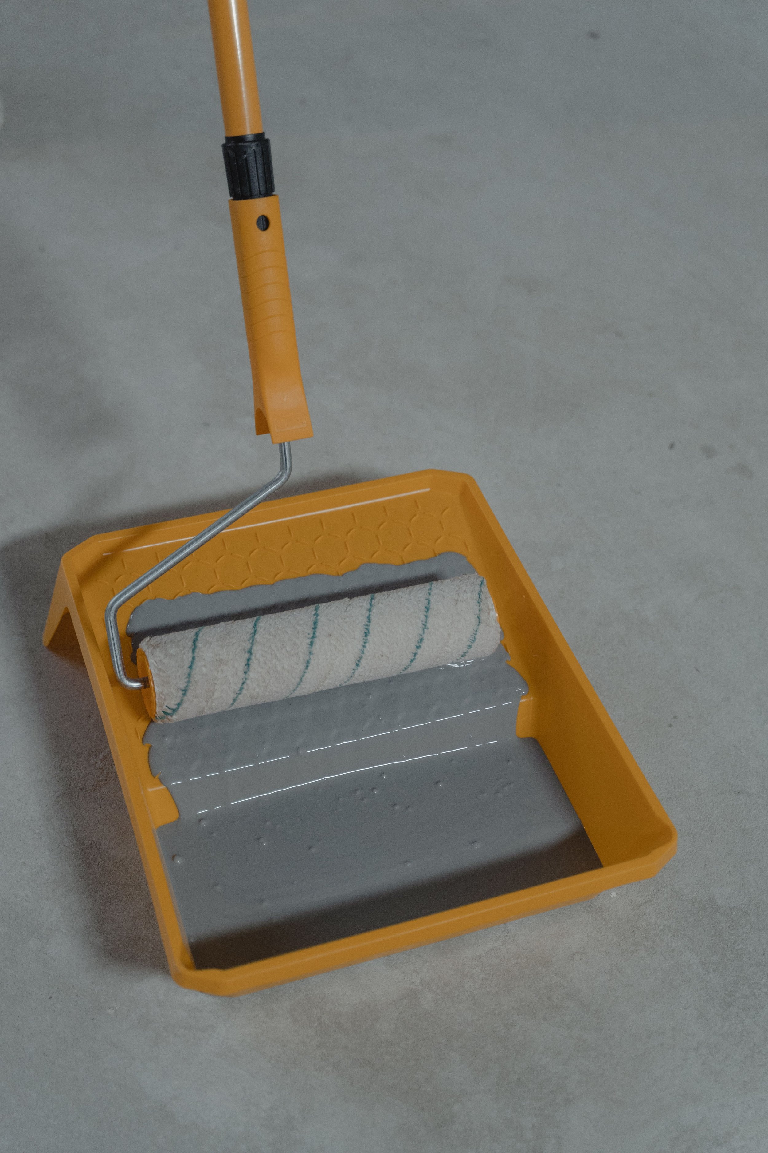 Yellow paint roller with a white roller cover on a yellow tray, resting on a concrete floor.