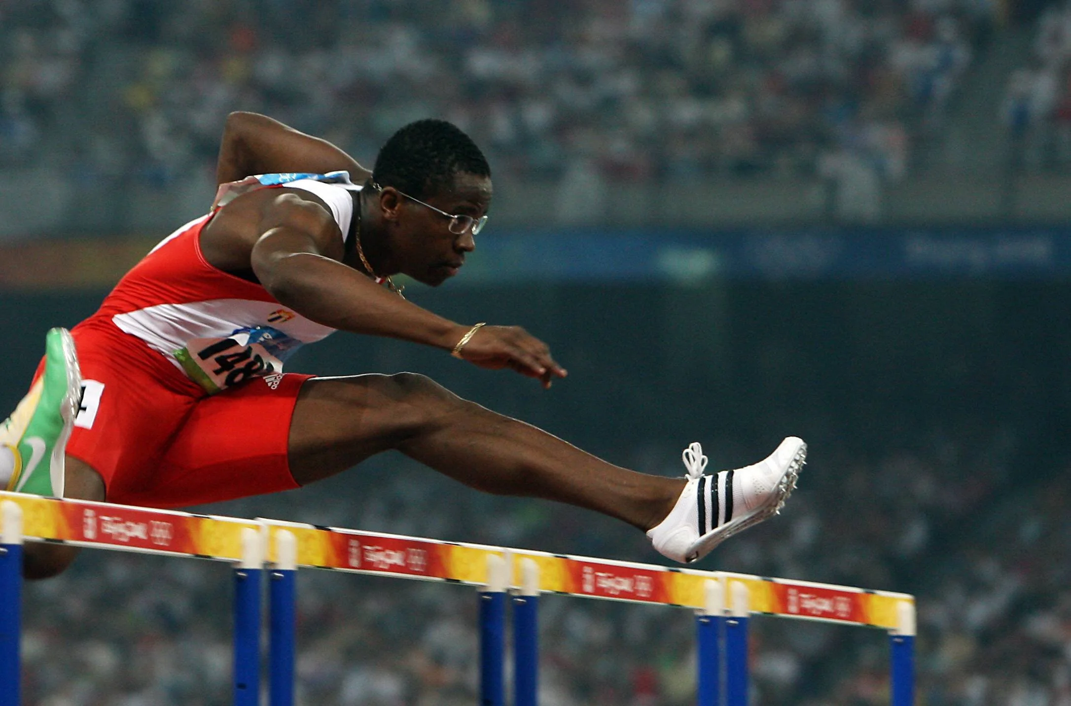 An athlete clears a hurdles race, mid-air, during a track and field event.