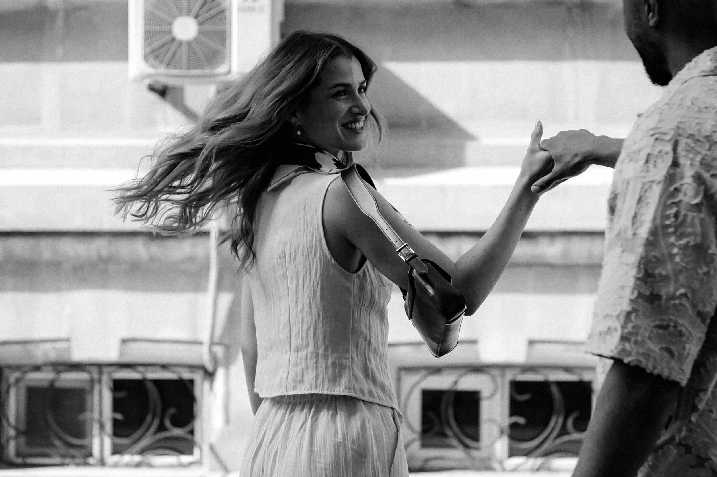A woman with long hair smiling and holding hands with a man in a casual setting, with laundry machines in the background.