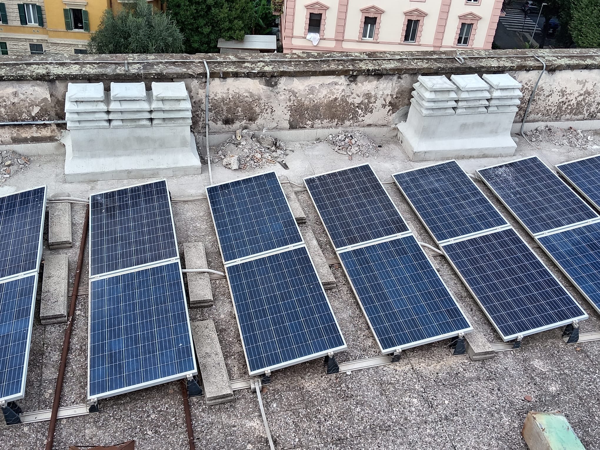 Pannelli solari installati sul tetto di un edificio in una zona urbana, con edifici colorati visibili sullo sfondo.