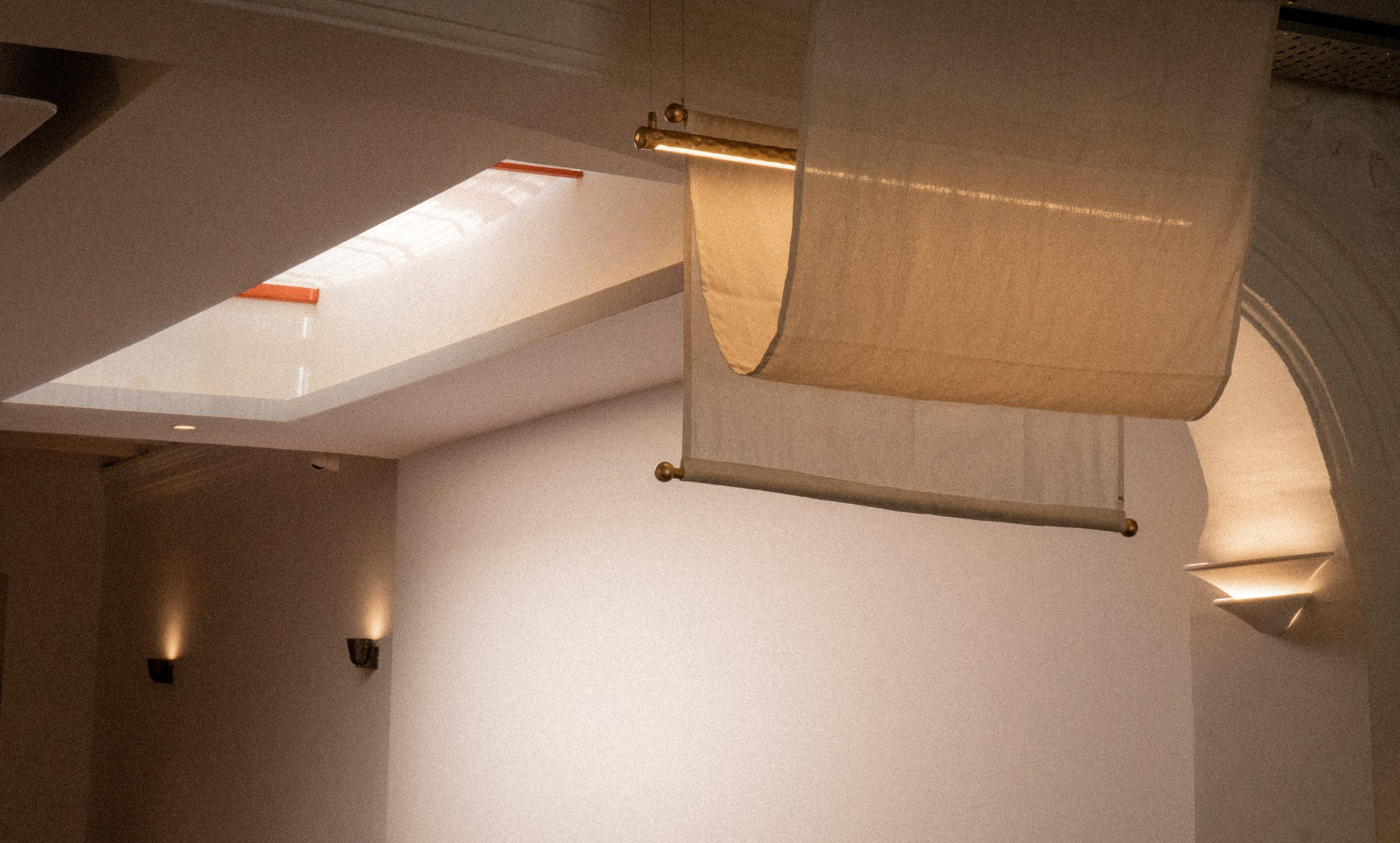 Interior view of a room with a ceiling skylight, a beige curtain hanging from a rod, and small wall-mounted lights.