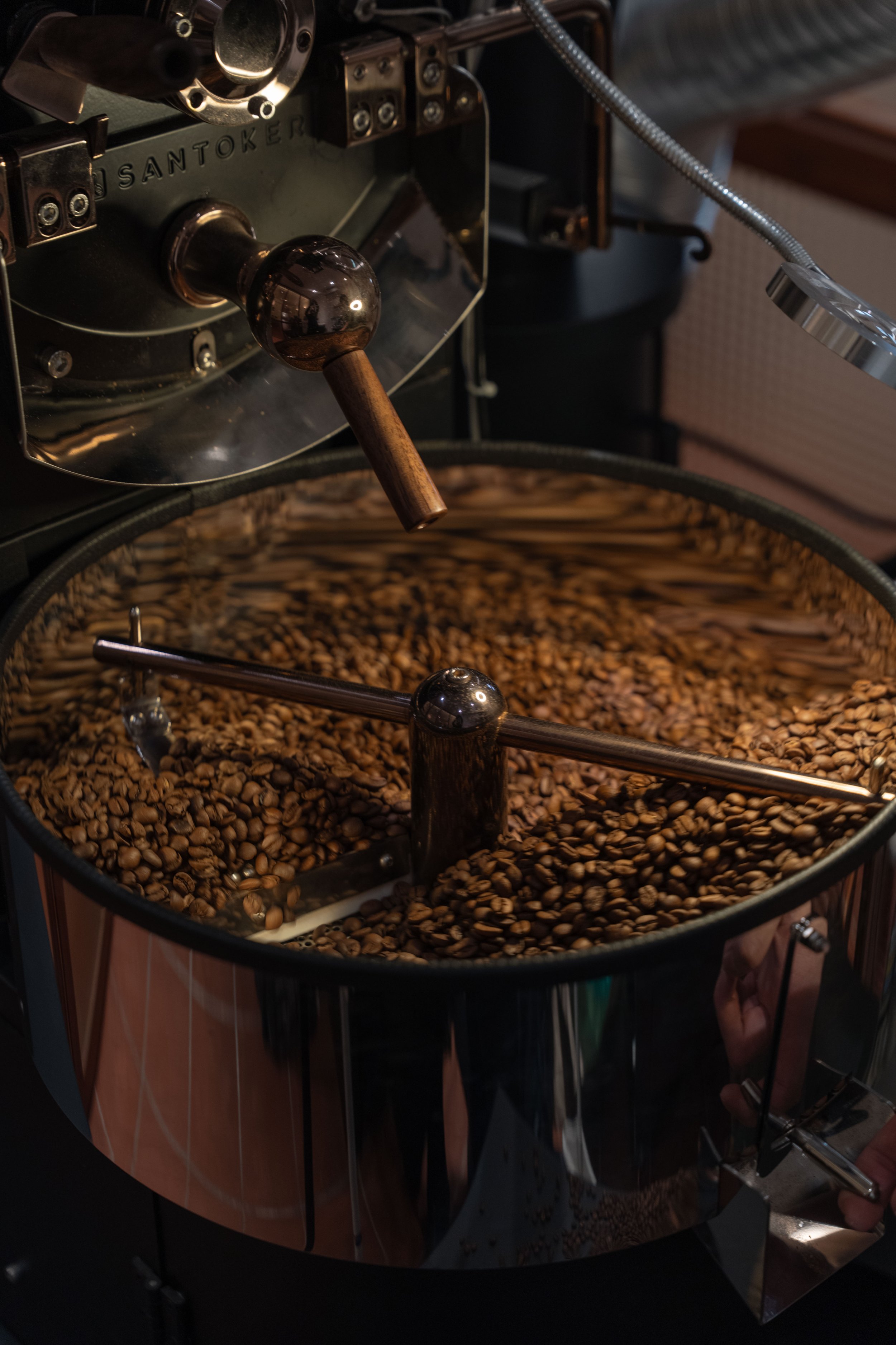 Coffee roaster machine with roasted coffee beans inside, visible controls and a reflective metal surface.