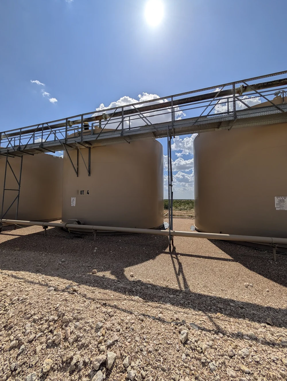 A row of tanks under an elevated steel walkway and pipe rack