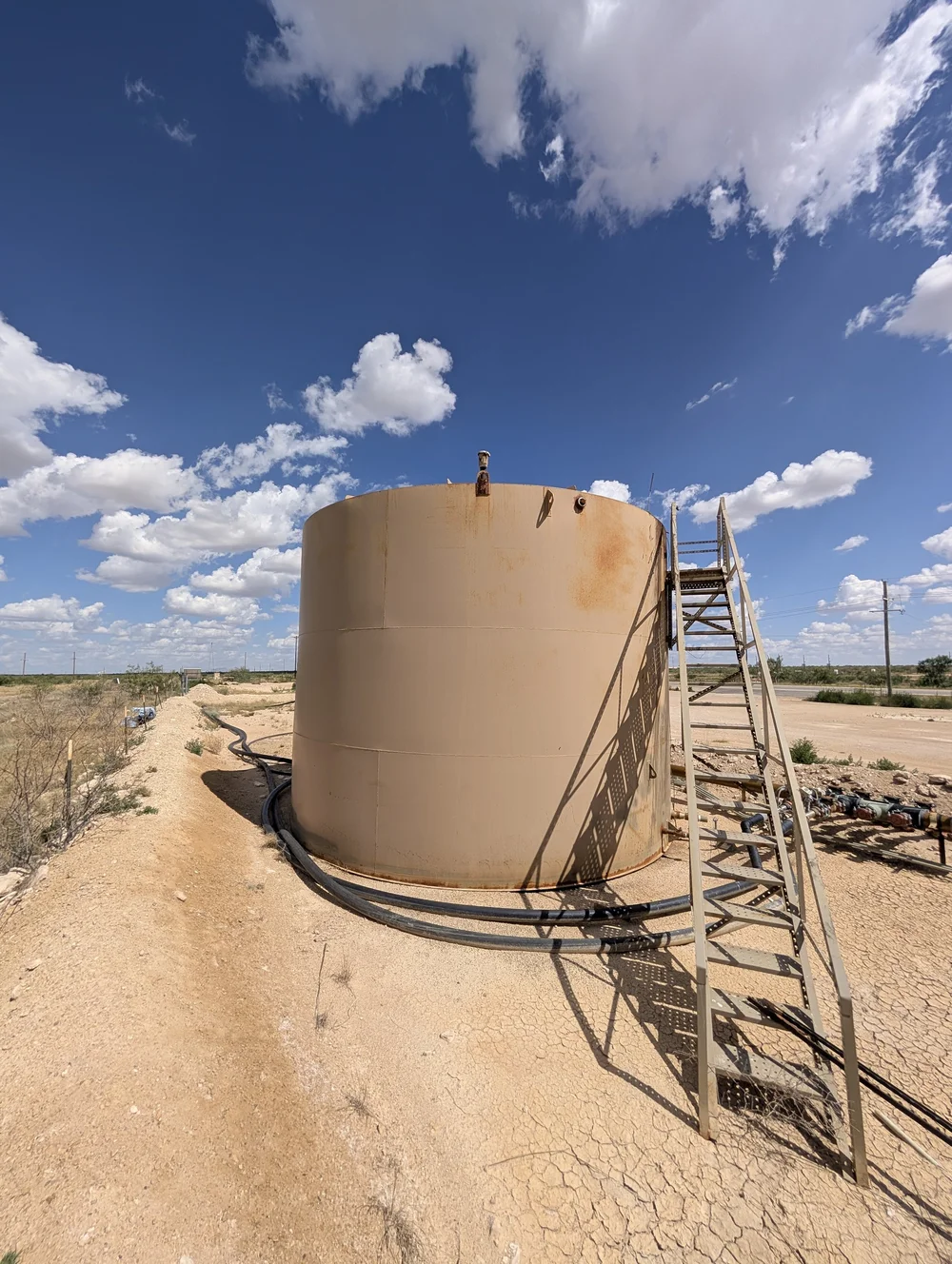 A single tank with rust staining on its upper courses and a steel stair to the roof