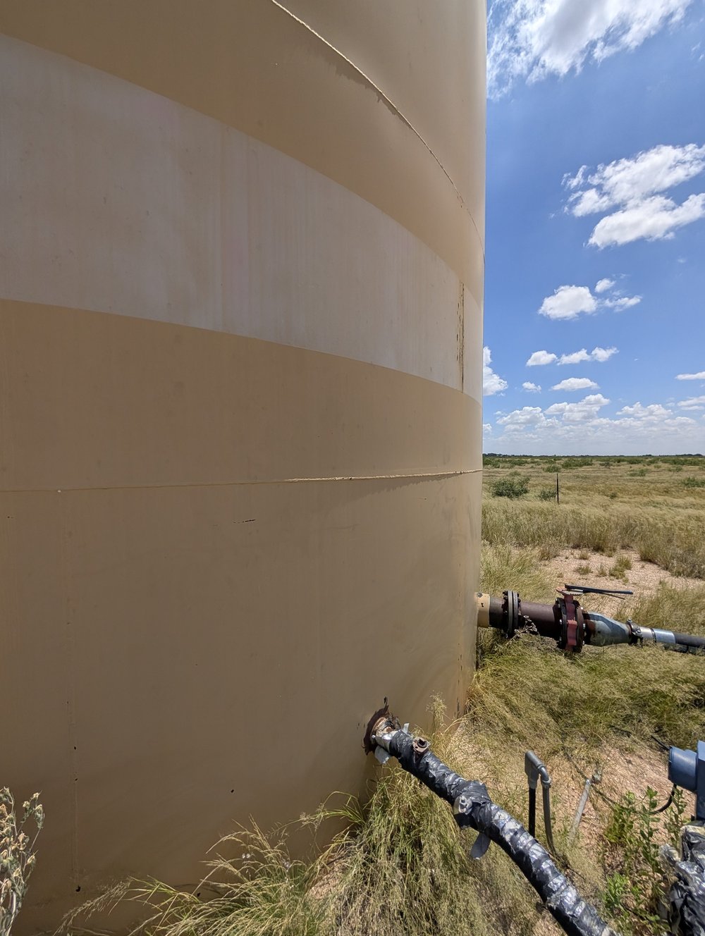 Close view of a tank shell with a horizontal weld seam and wrapped pipework entering the bottom course
