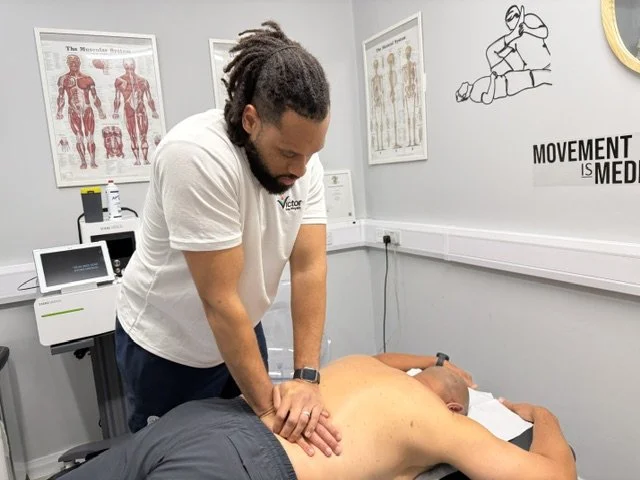 A male physiotherapist giving a back massage to a person lying face down on a medical treatment table in a physiotherapy clinic room.