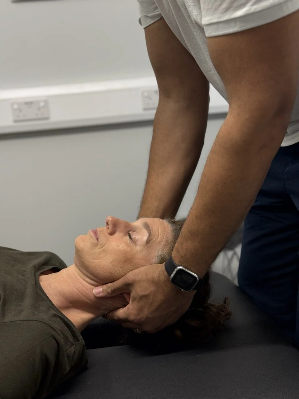 Person receiving a neck adjustment or massage from a physiotherapist in a clinical setting.