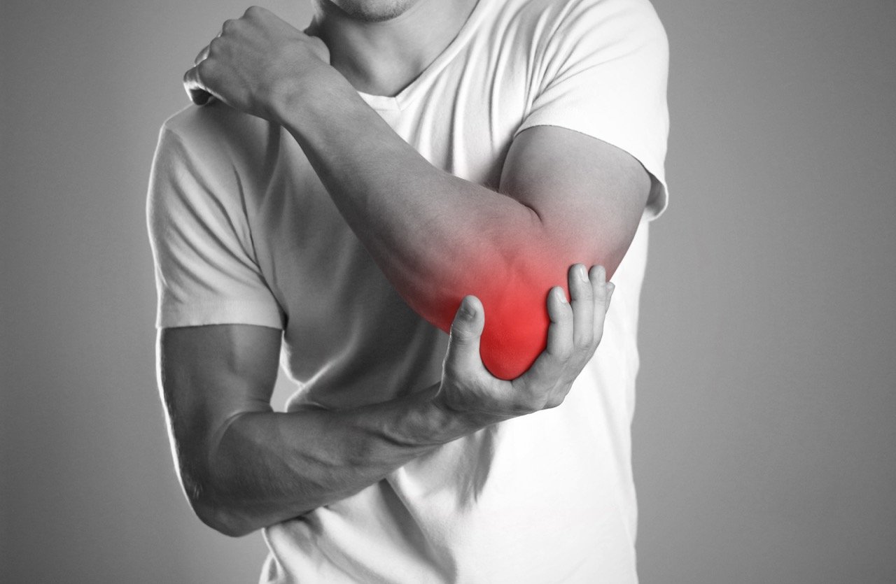 A person in a t-shirt grabbing their elbow with pain highlighted in red, indicating arm discomfort or injury.