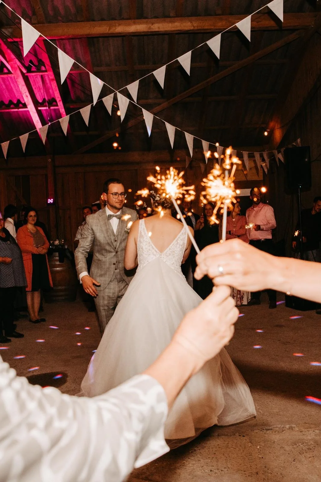 Hochzeitspaar tanzt im festlich dekorierten Raum, Besucher beobachten, im Vordergrund halten Gäste Funkenfackeln. Bunte Lichter und weiße Girlanden schmücken die Decke.
