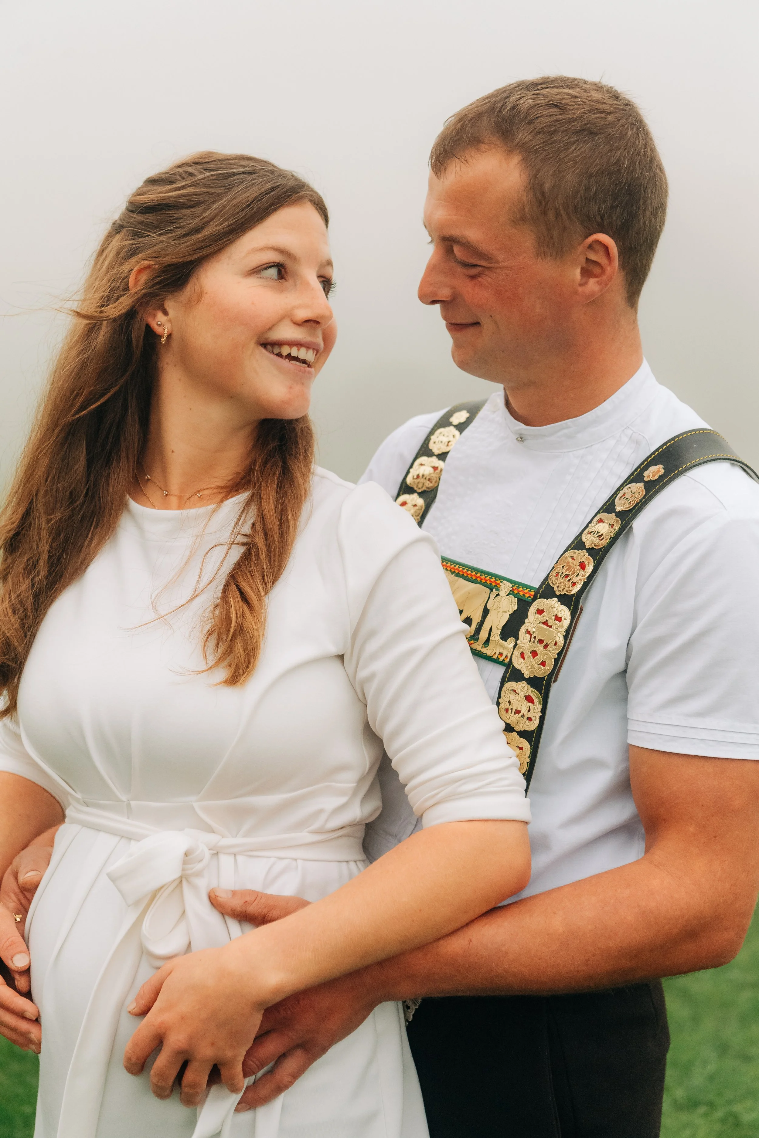 Ein Paar in traditioneller Kleidung, das eine Frau in einem weißen Kleid und ein Mann in Tracht umarmt.