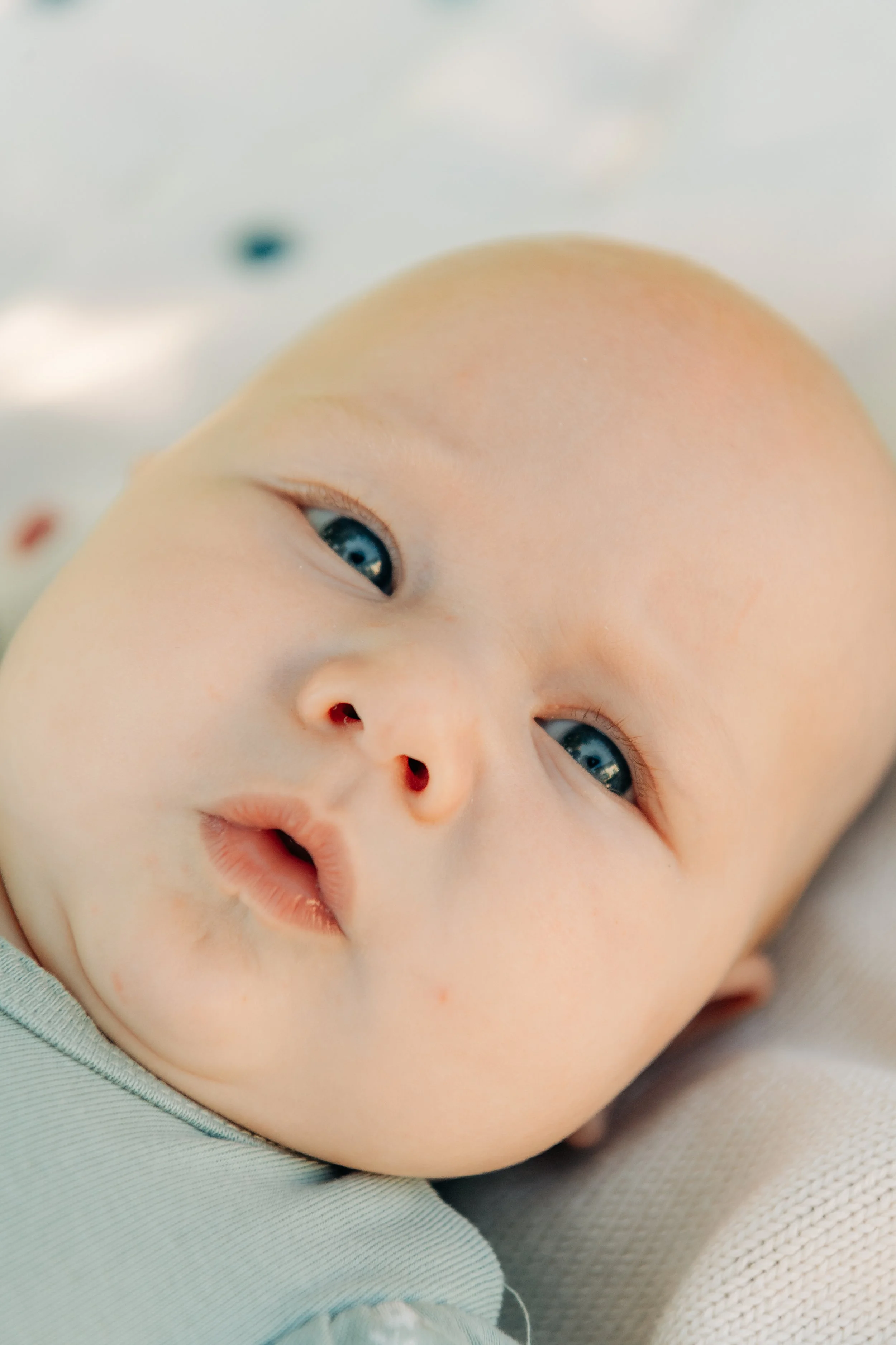 Nahaufnahme eines Babys mit blauen Augen, das auf einem weichen, hellgrauen Stoff liegt.