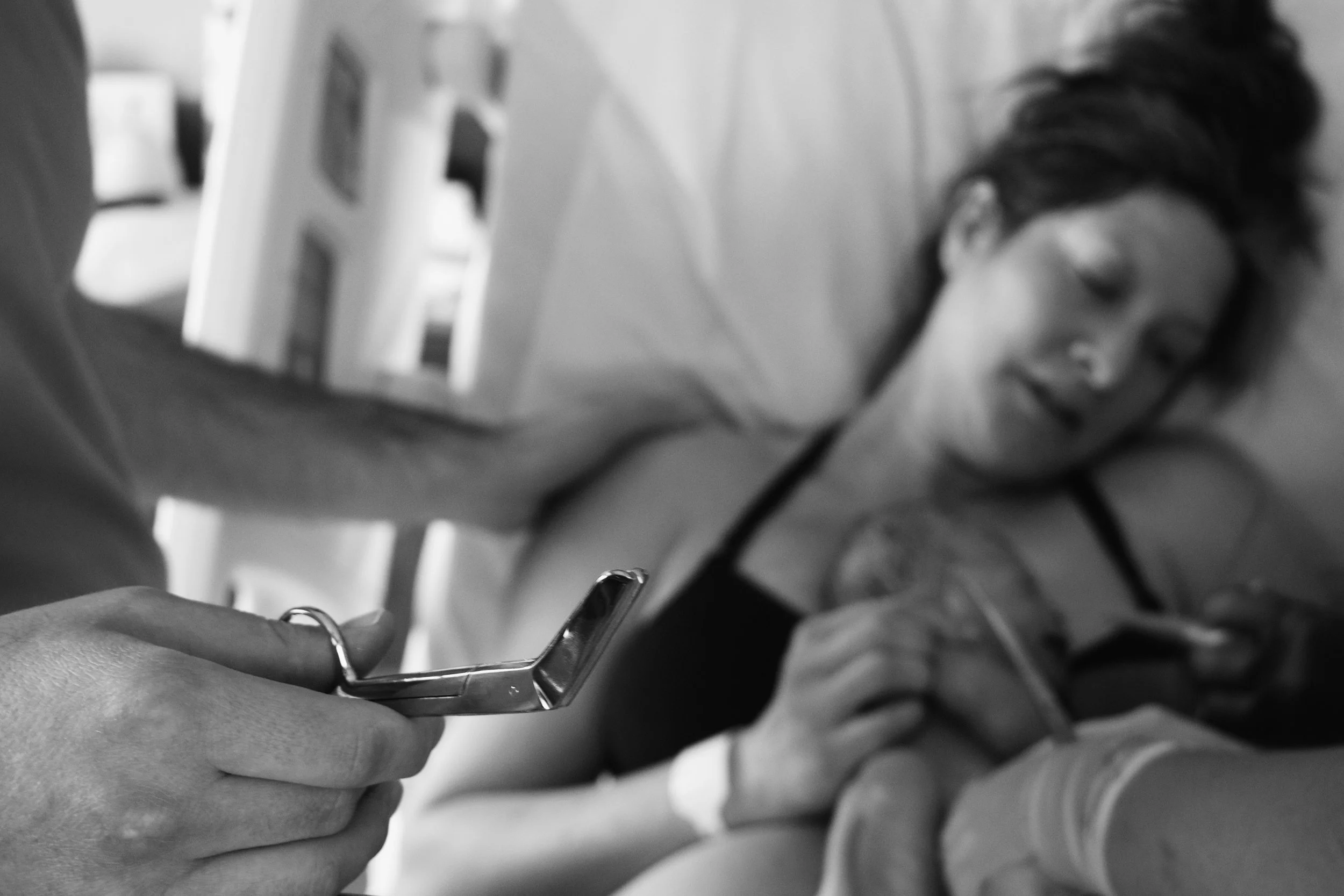 A person holding a smartphone while resting their head on a pillow, with a woman sleeping nearby in a dimly lit room.