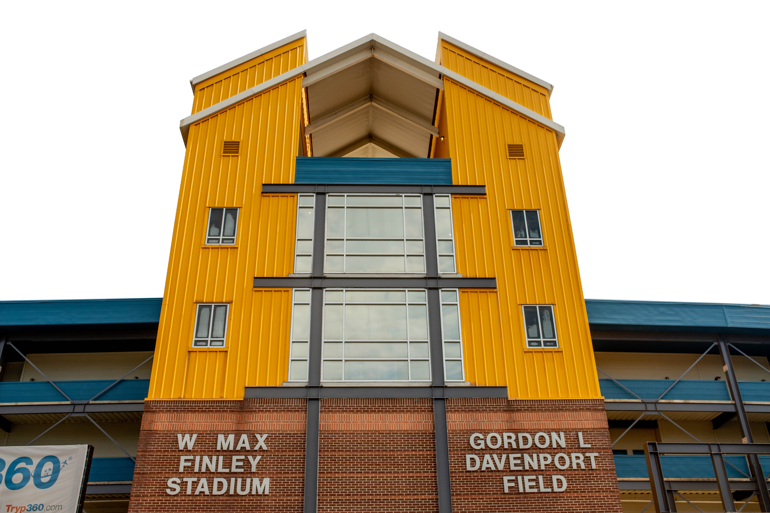 A multi-story building with yellow and blue exterior walls, large windows, and signs indicating it is associated with Gordon Davenport Field and Finley Stadium, with a clear sky in the background.