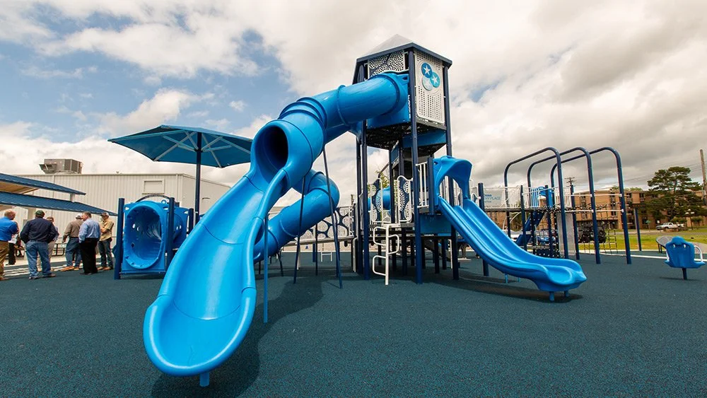 Blue playground structure with slides and tunnels at a park, with people in the background.