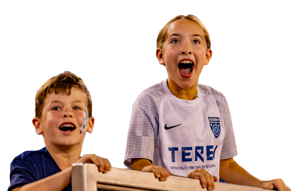 Two kids with painted faces, wearing sports jerseys, holding a wooden stick, smiling and cheering.