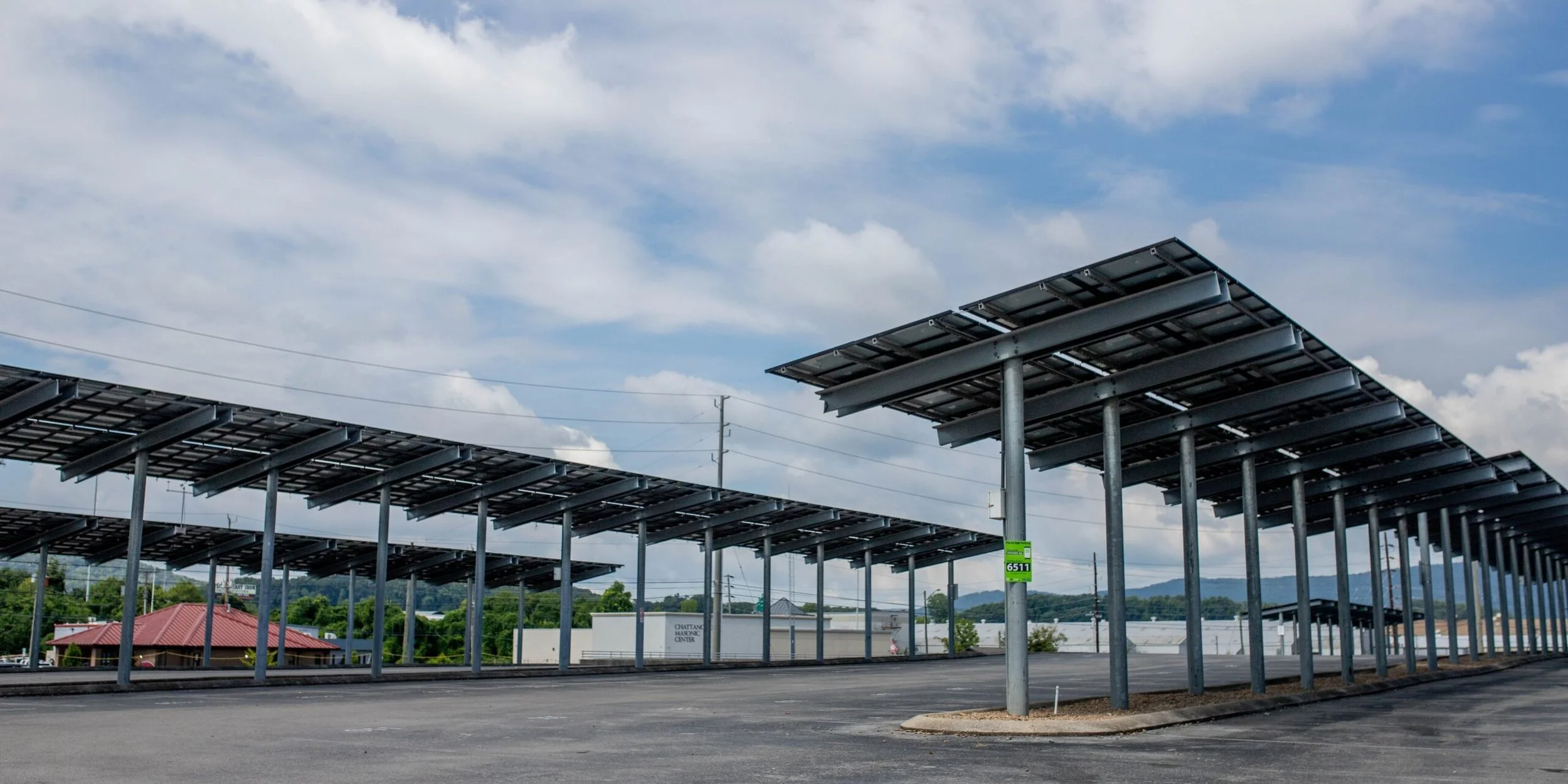 Solar panels installed on metal structures in an outdoor parking lot, with a partly cloudy sky in the background.