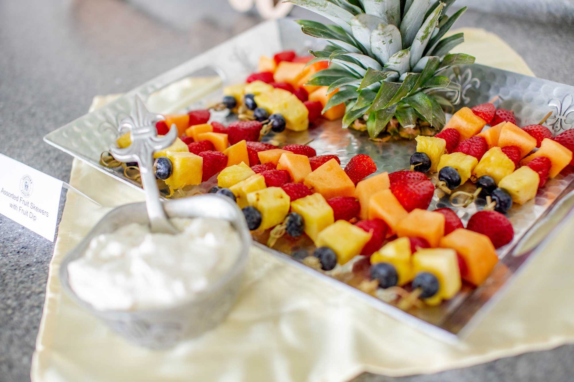 A silver tray of assorted fruit skewers with a pineapple on the side.