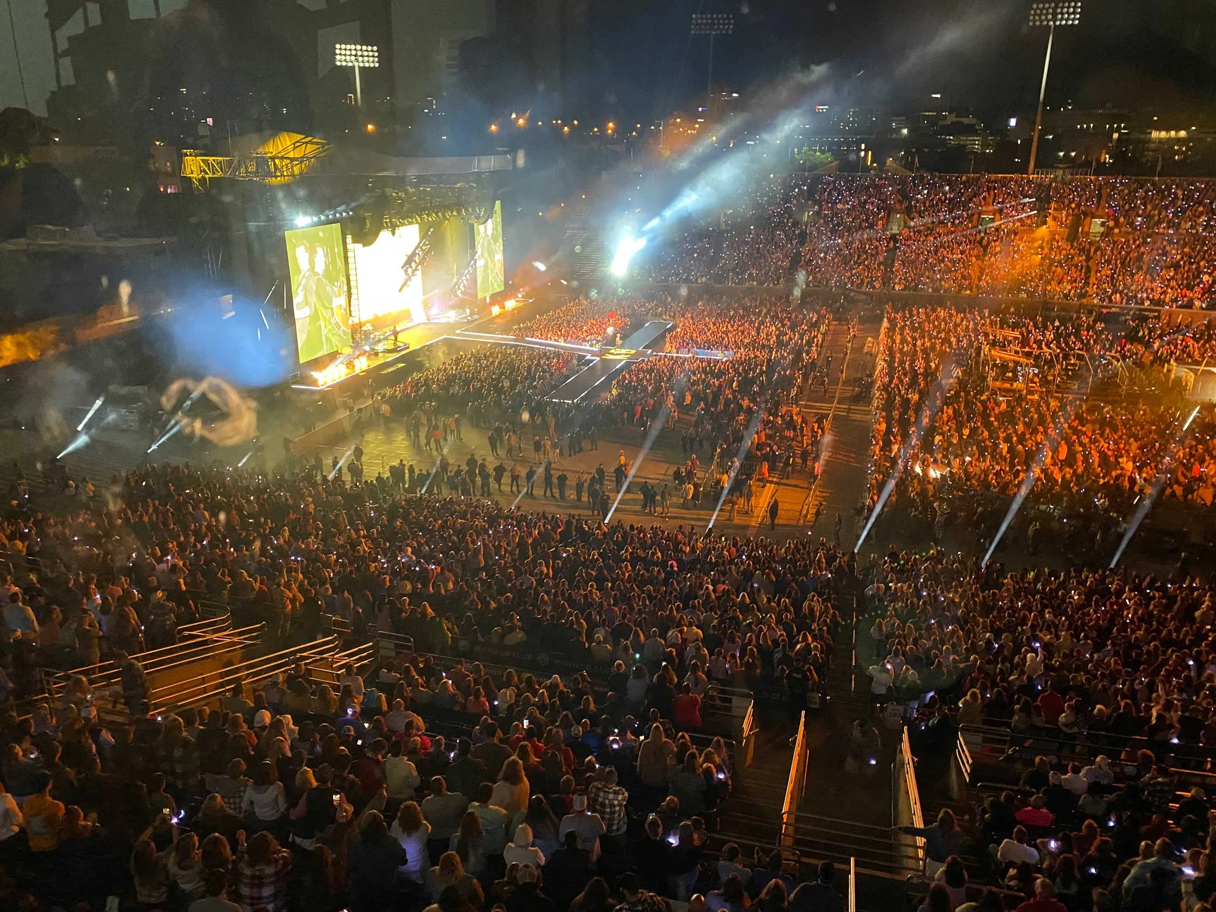 A concert at night with a large crowd, stage lighting, and big screens showing performers.