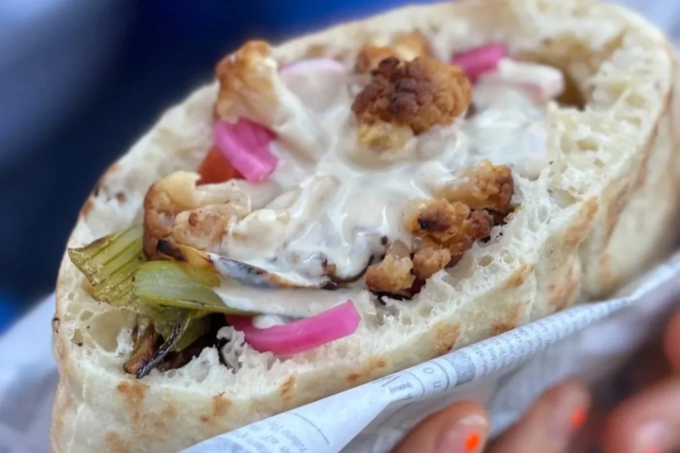 Close-up of a gyros sandwich with pita bread, topped with grilled chicken, onions, pickles, and creamy sauce.